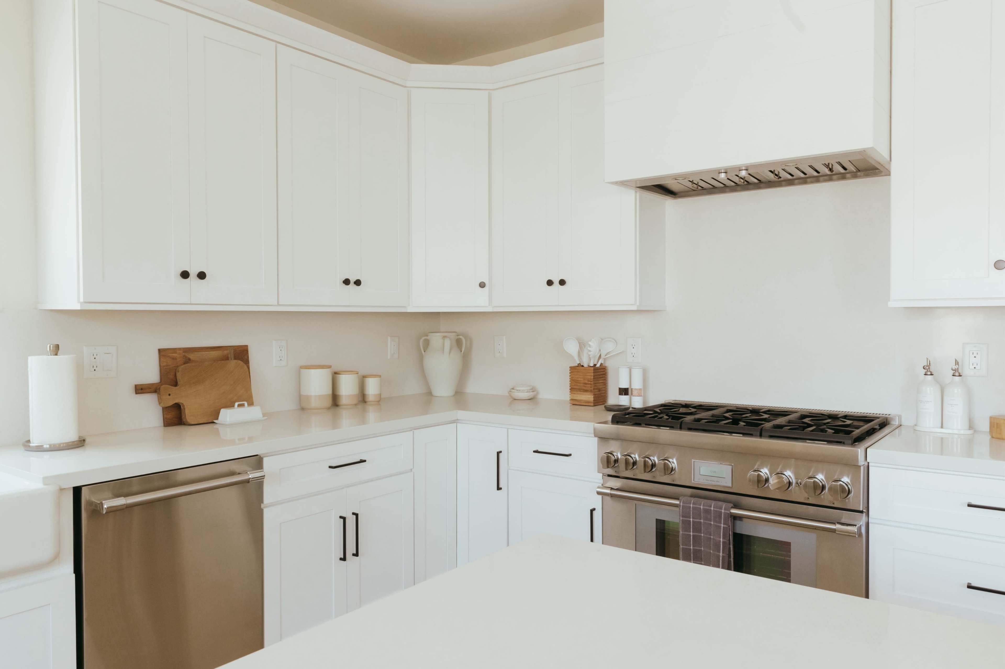 A modern kitchen with white cabinetry, a stainless steel stove, and a neutral countertop.