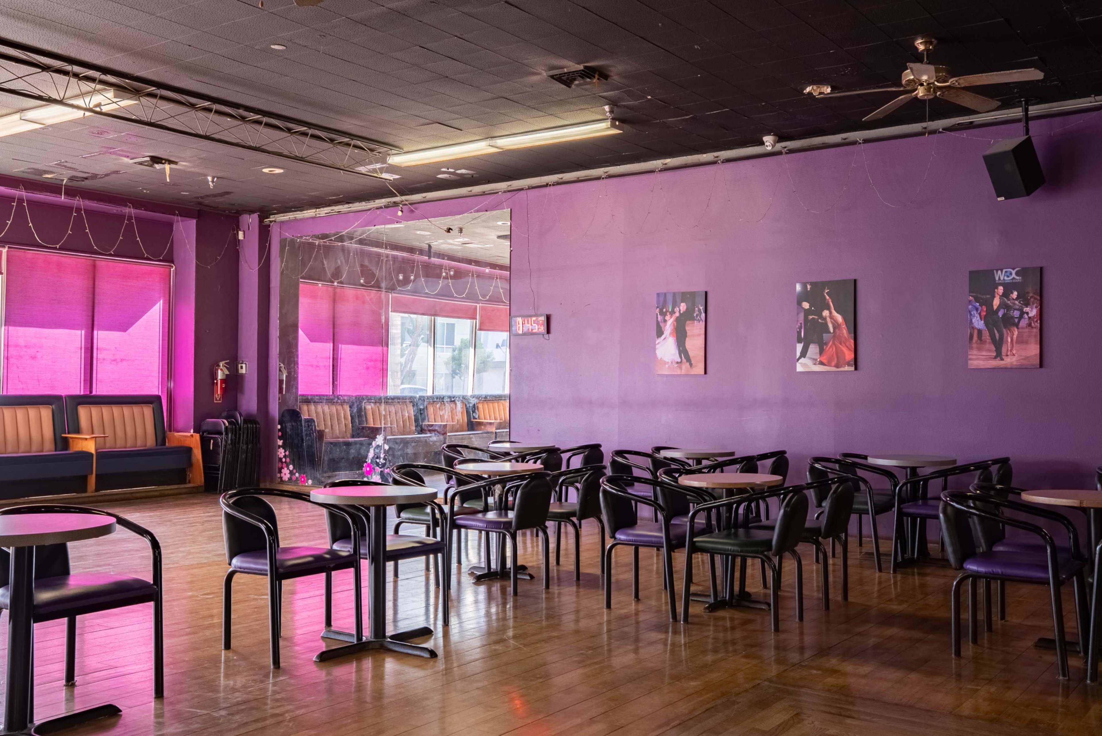 The image shows a spacious indoor venue with purple walls, wooden flooring, and several tables and chairs arranged for seating.