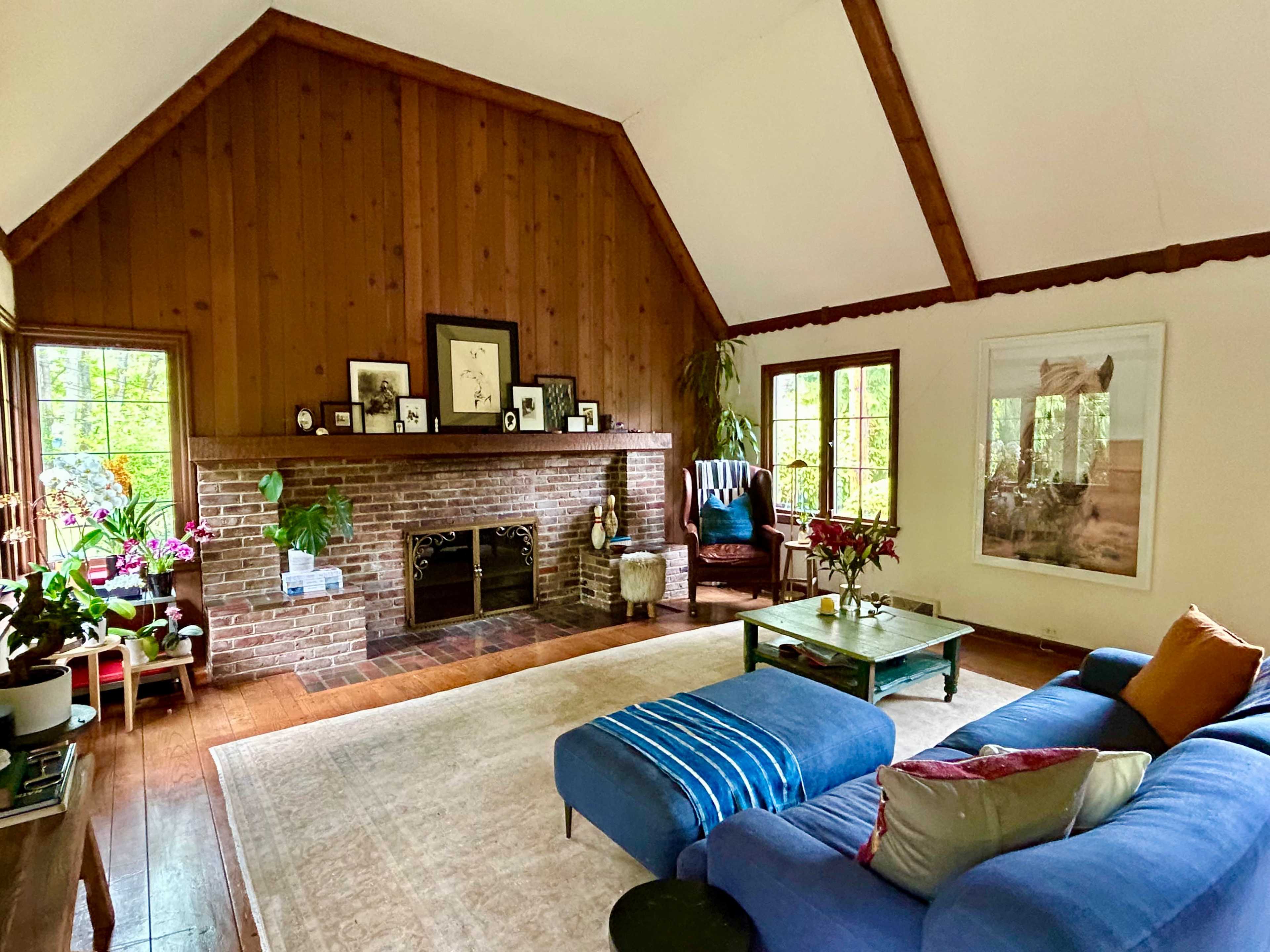 The living room features a vaulted wooden ceiling, a brick fireplace with a mantel, and a blue sectional sofa arranged around a coffee table.