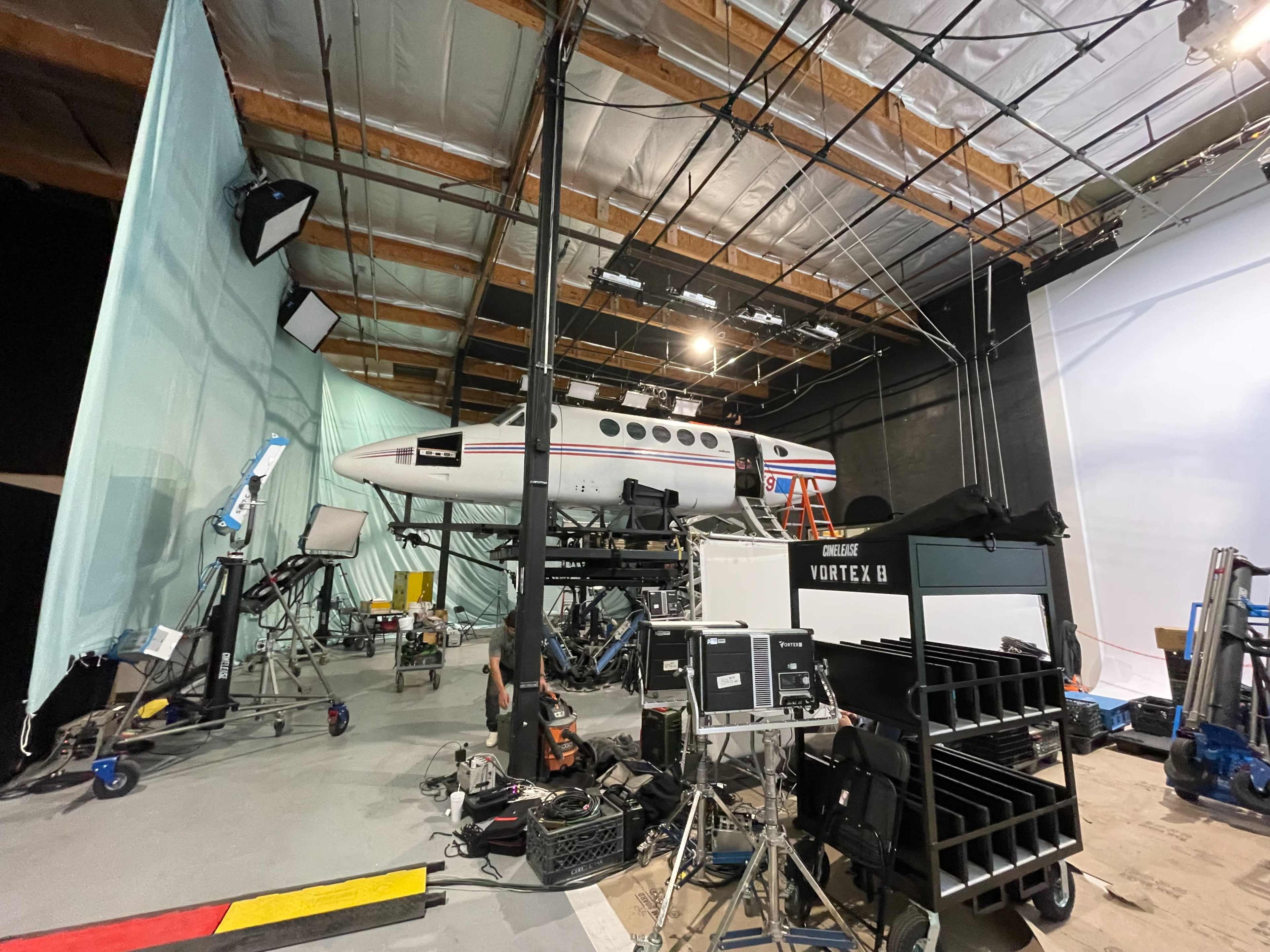 A private aircraft is positioned on a movie set surrounded by film equipment and lighting.