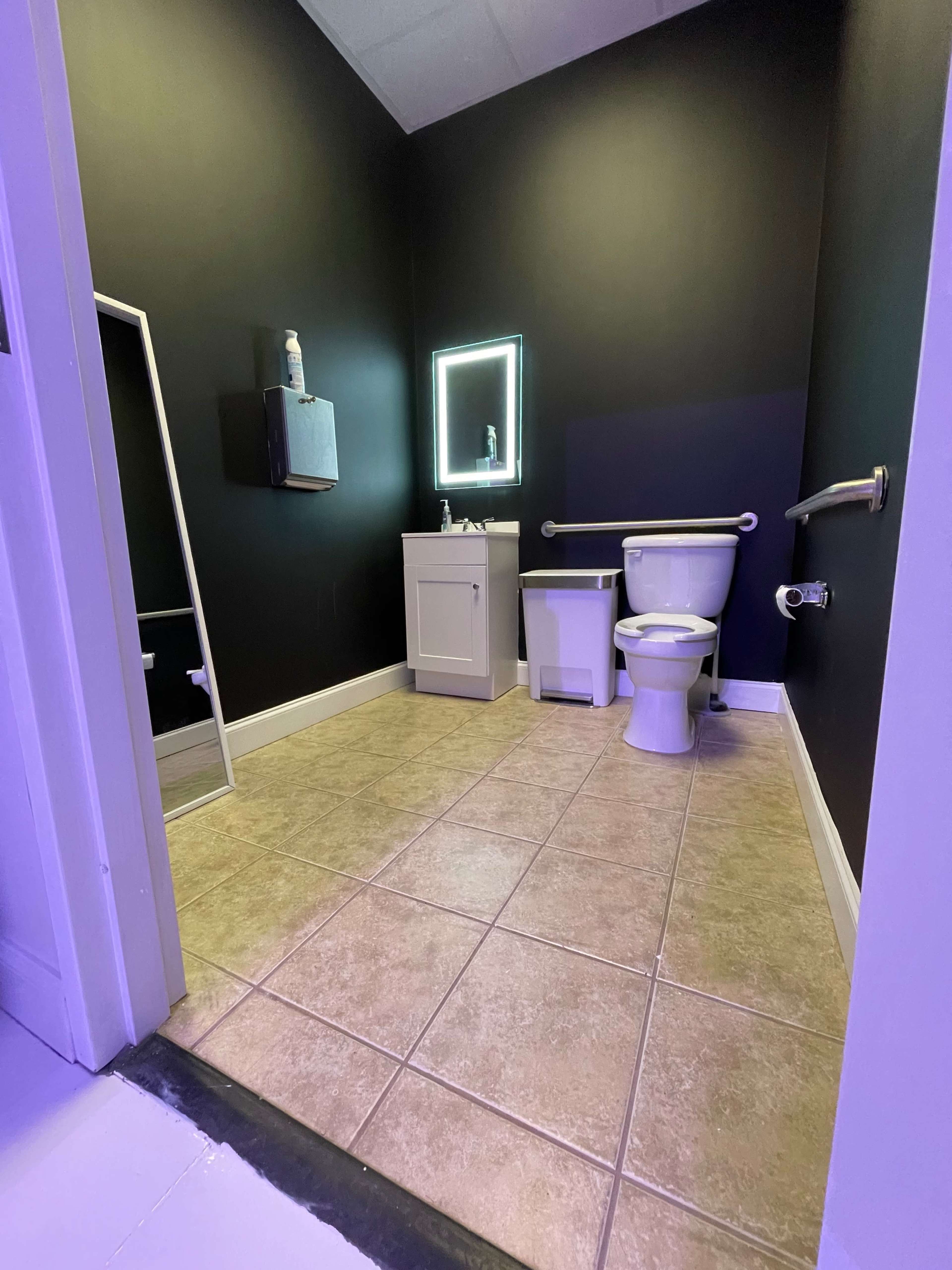A modern bathroom with black walls, a mirror, a toilet, a sink, and tiled flooring.