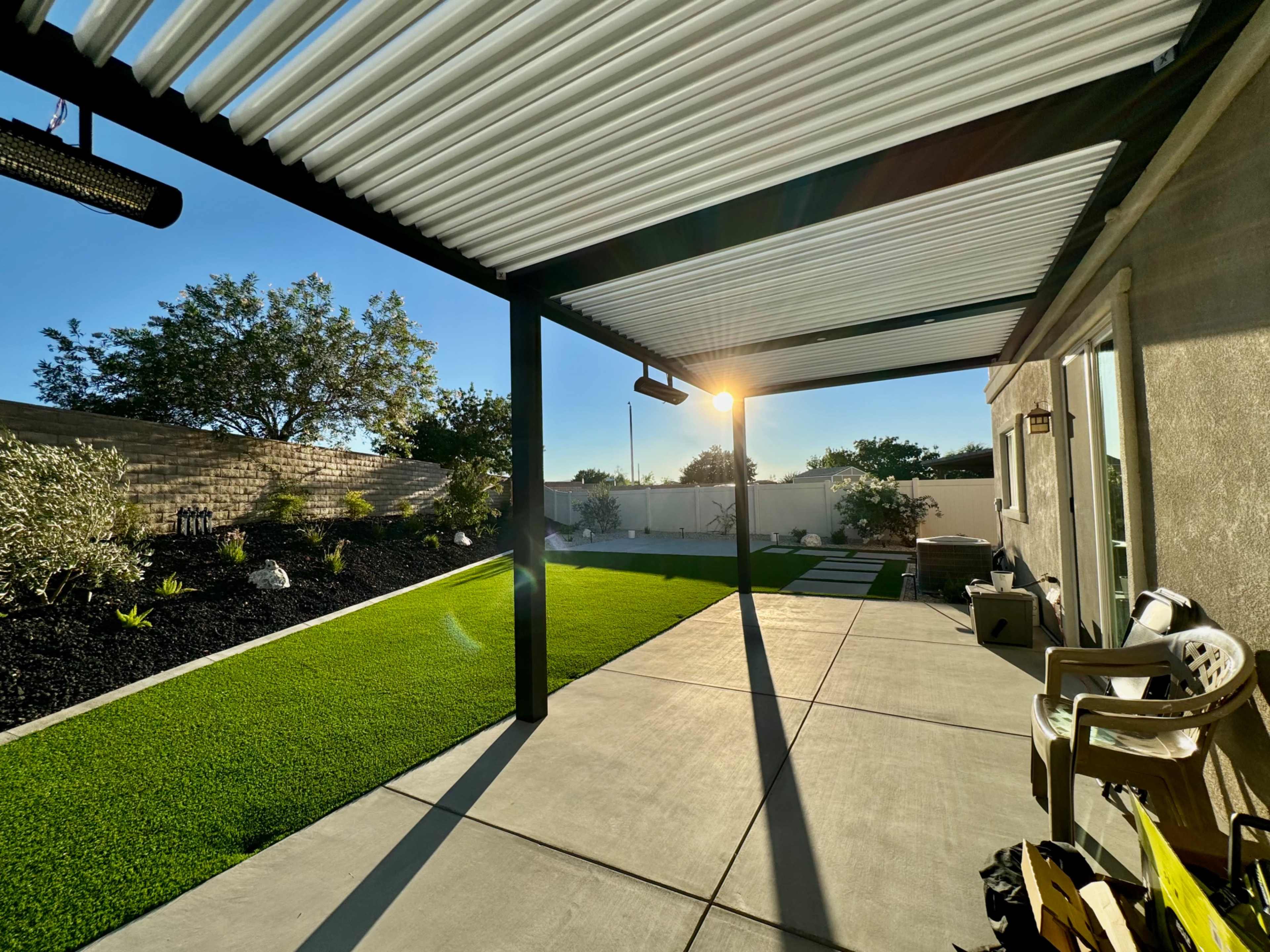 A patio with a pergola and green grass is illuminated by the late afternoon sun.