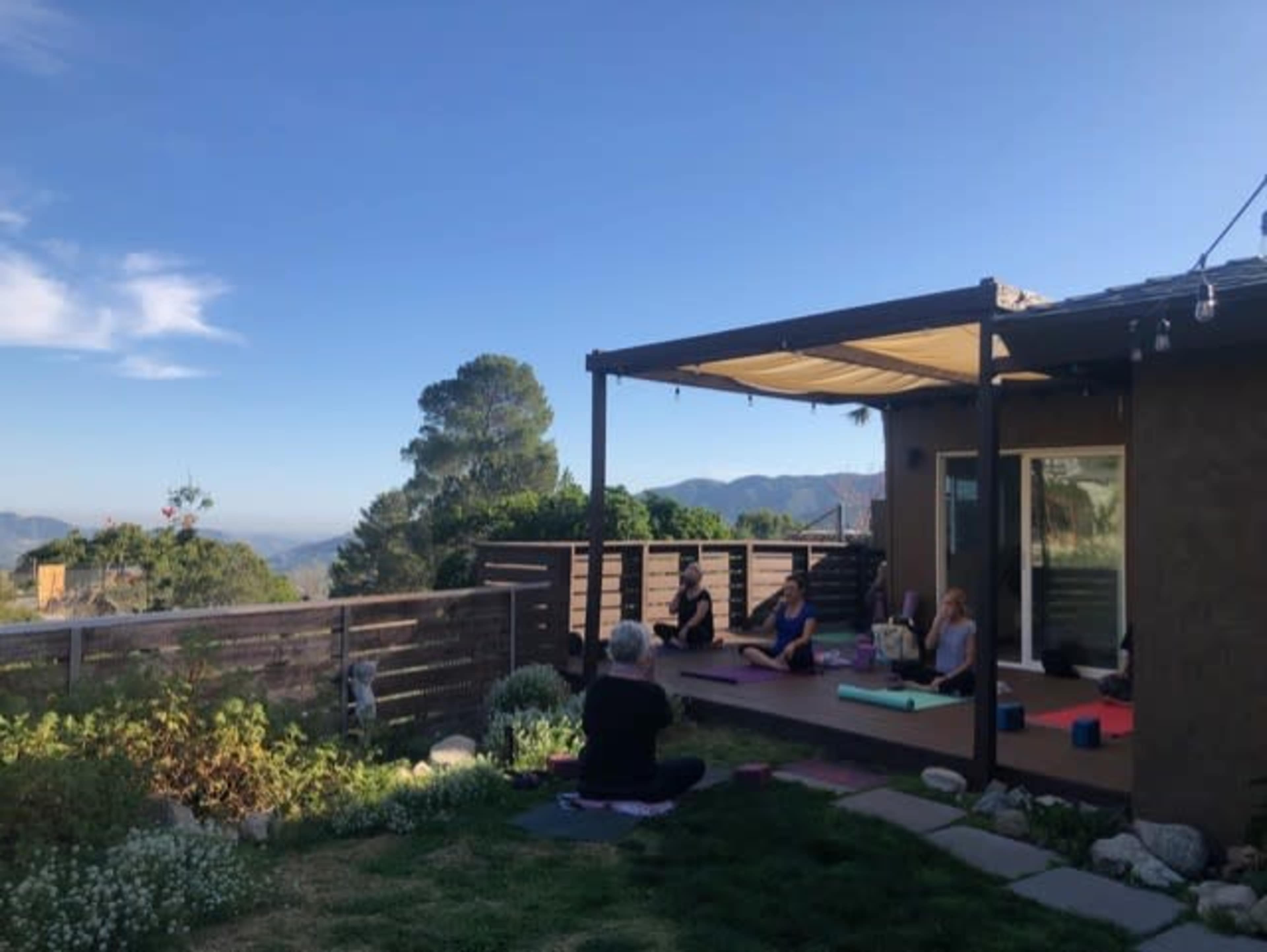 A group of people practice yoga on a deck overlooking a mountainous landscape.