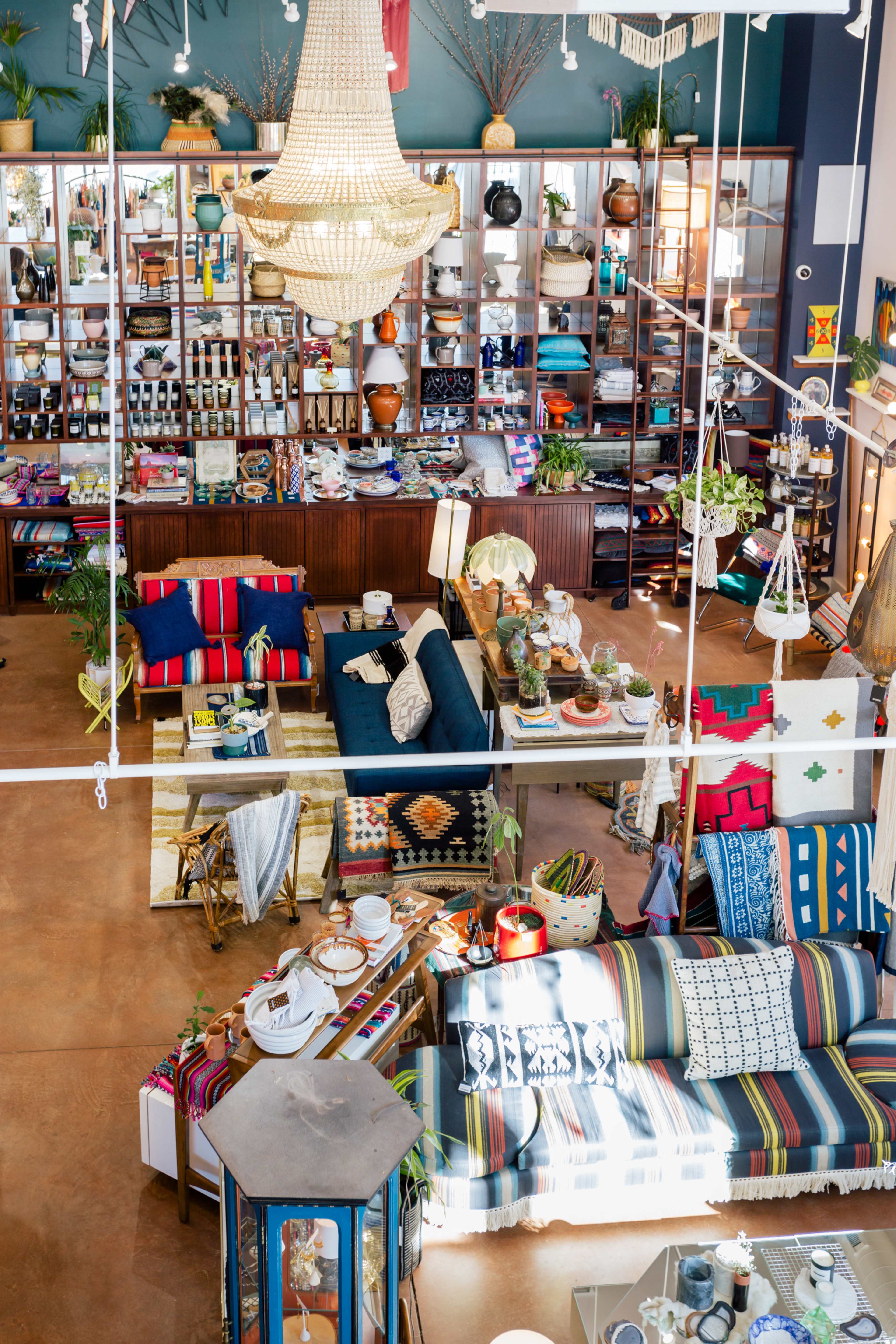 A bright, spacious store filled with various decorative items, furniture, and textiles, highlighted by a large chandelier and multiple display shelves.