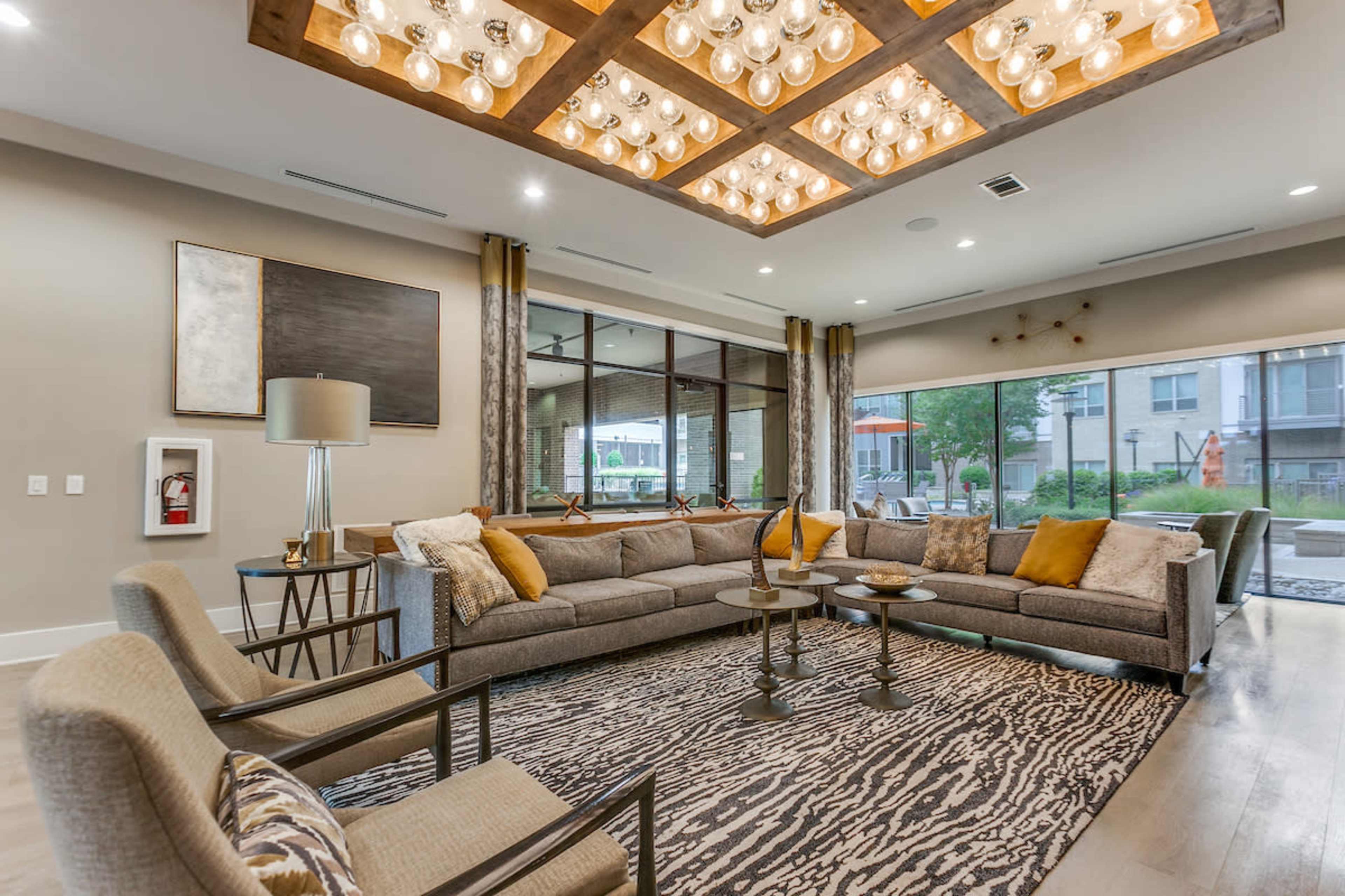 A spacious and modern communal living area with a large sectional sofa, decorative lighting, and large windows overlooking an outdoor space.