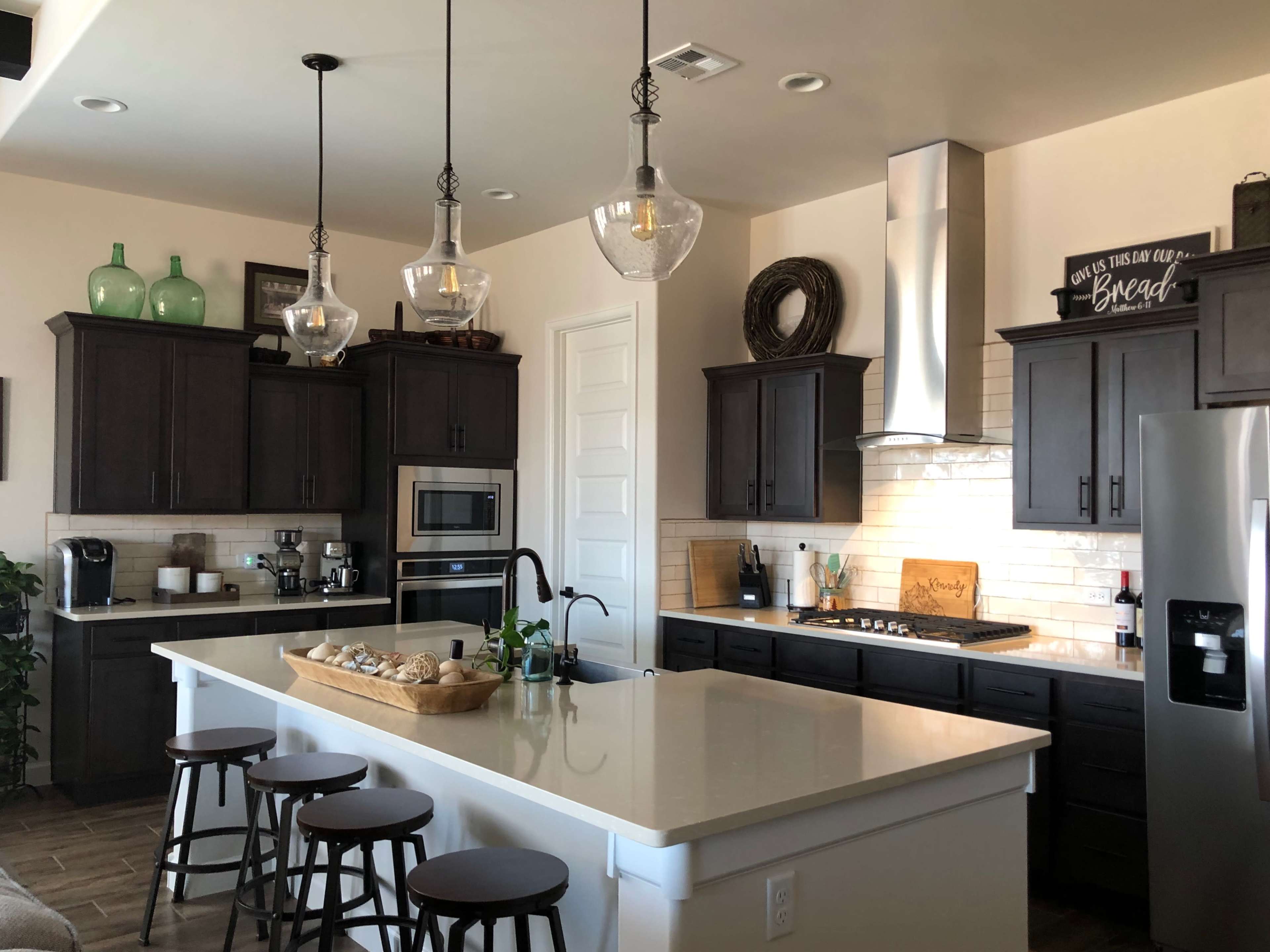 The image depicts a modern kitchen featuring dark wooden cabinets, a central island with a basket of bread, and stainless steel appliances.