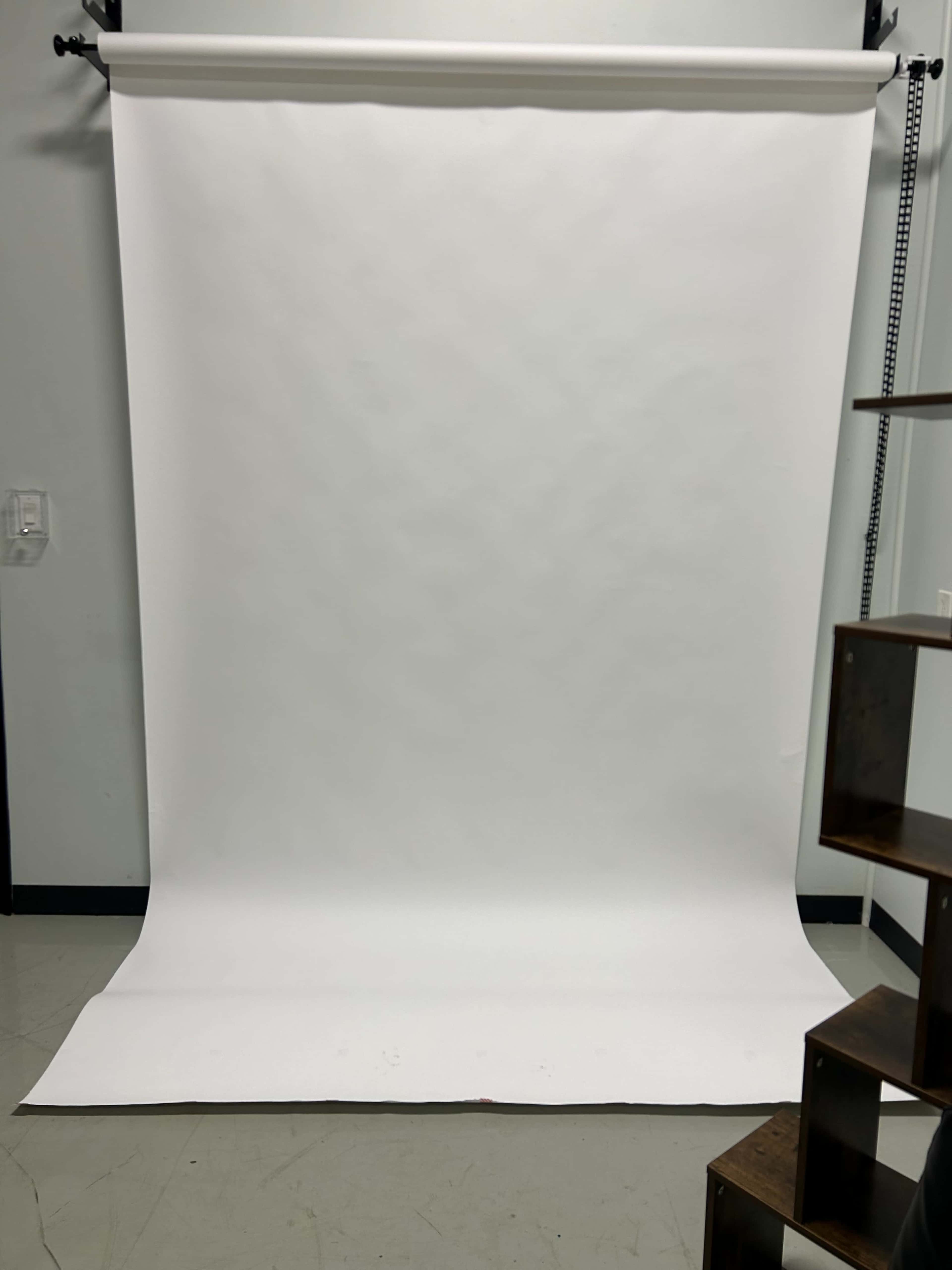 The image shows a plain, white backdrop in a studio setting, with a wooden structure positioned on the right side.
