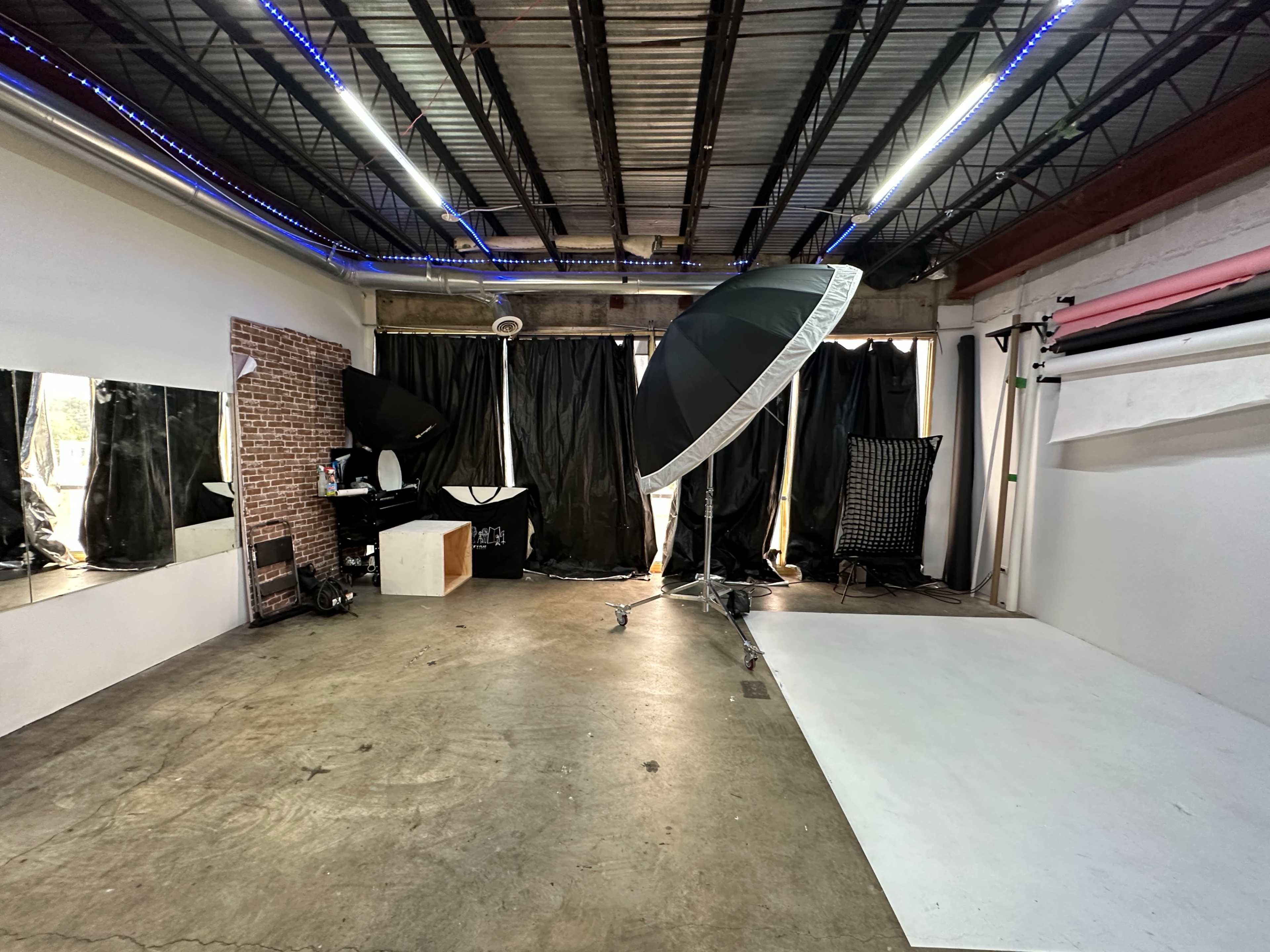 A photography studio featuring a white backdrop, large softbox light, mirrors, and black curtains.