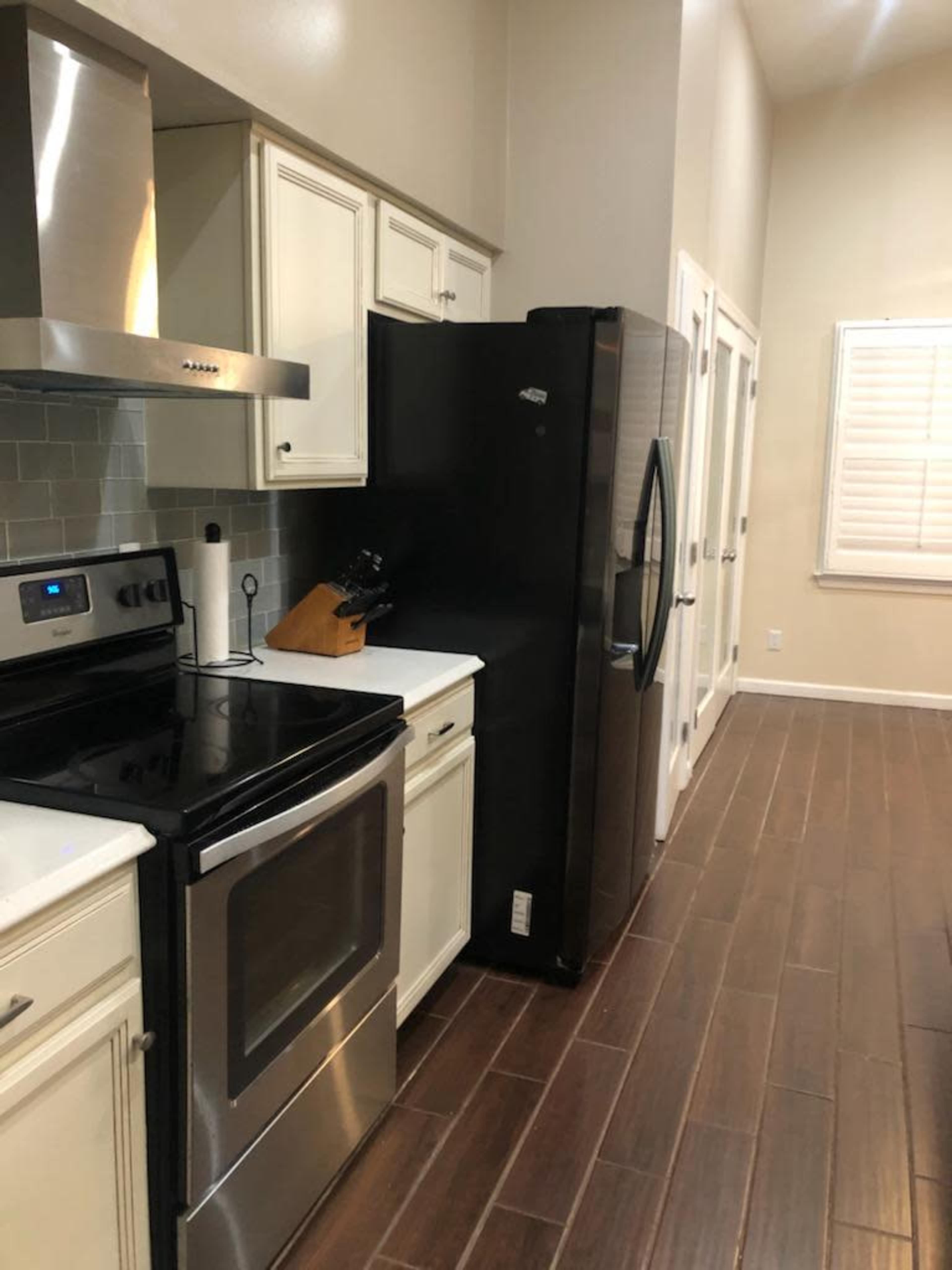 A modern kitchen with stainless steel appliances, including an oven and a refrigerator, along a wooden floor with beige walls.
