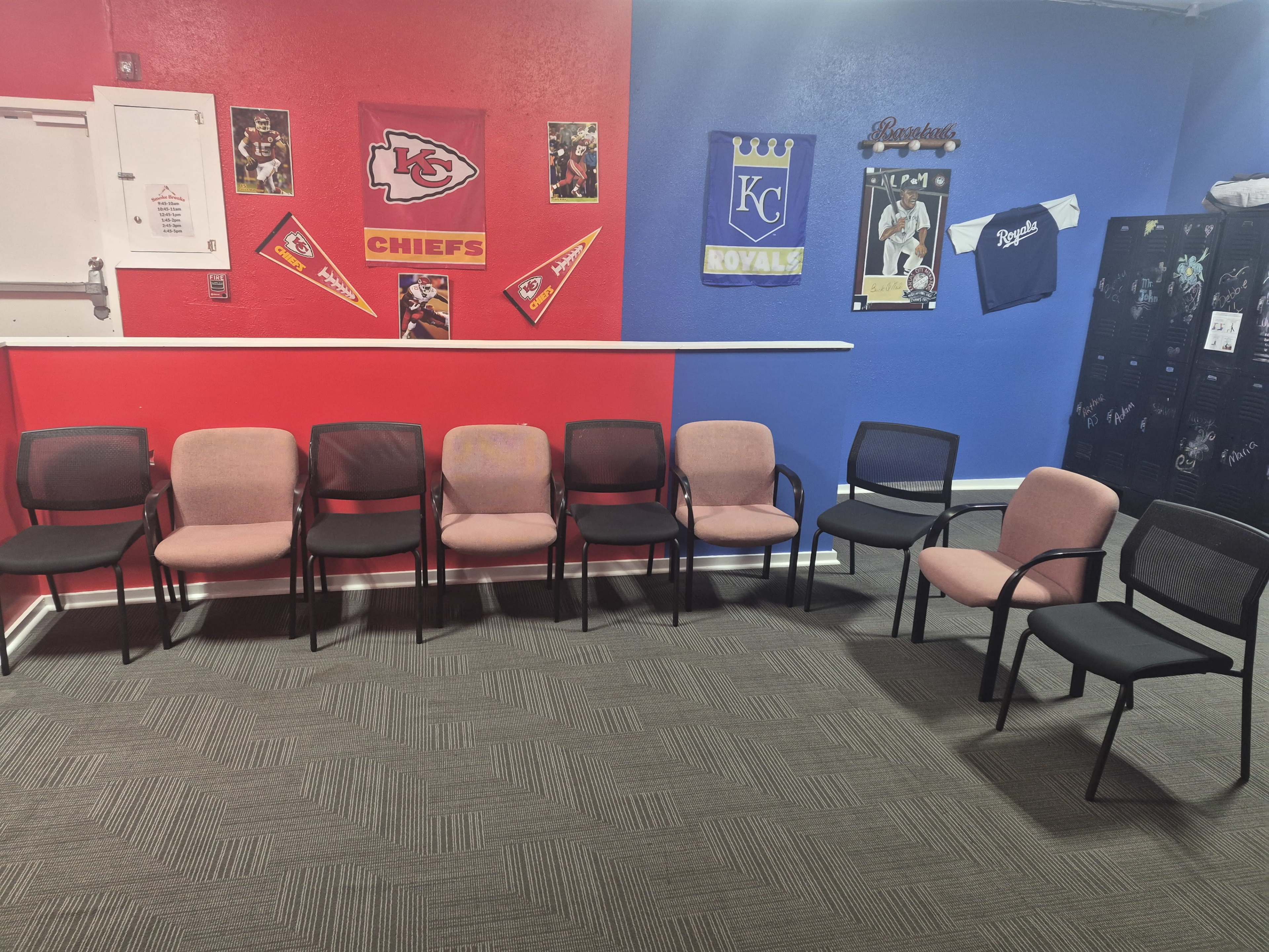 The image shows a waiting area with a row of chairs against a red and blue wall, decorated with sports memorabilia, including jerseys and team banners.