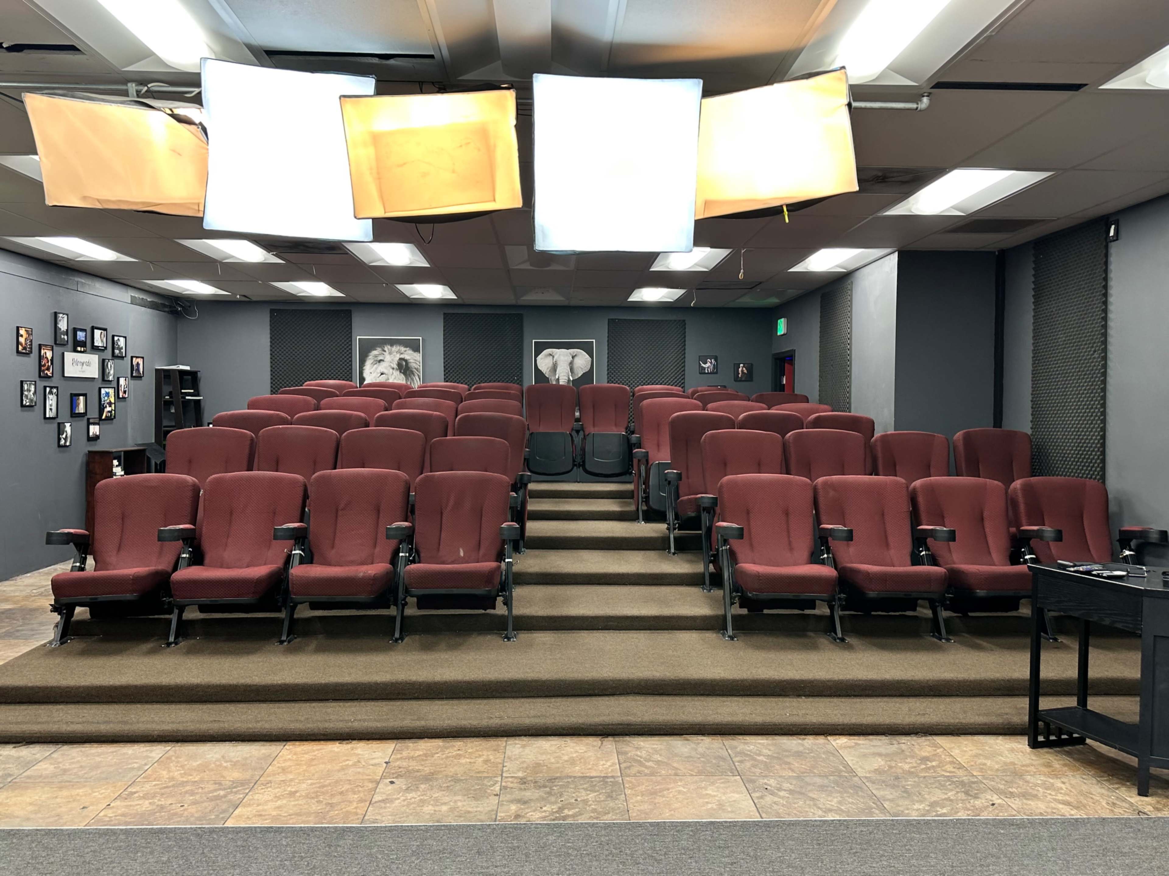 A small theater with red seats arranged in rows on a raised platform, surrounded by dark walls and ambient lighting.
