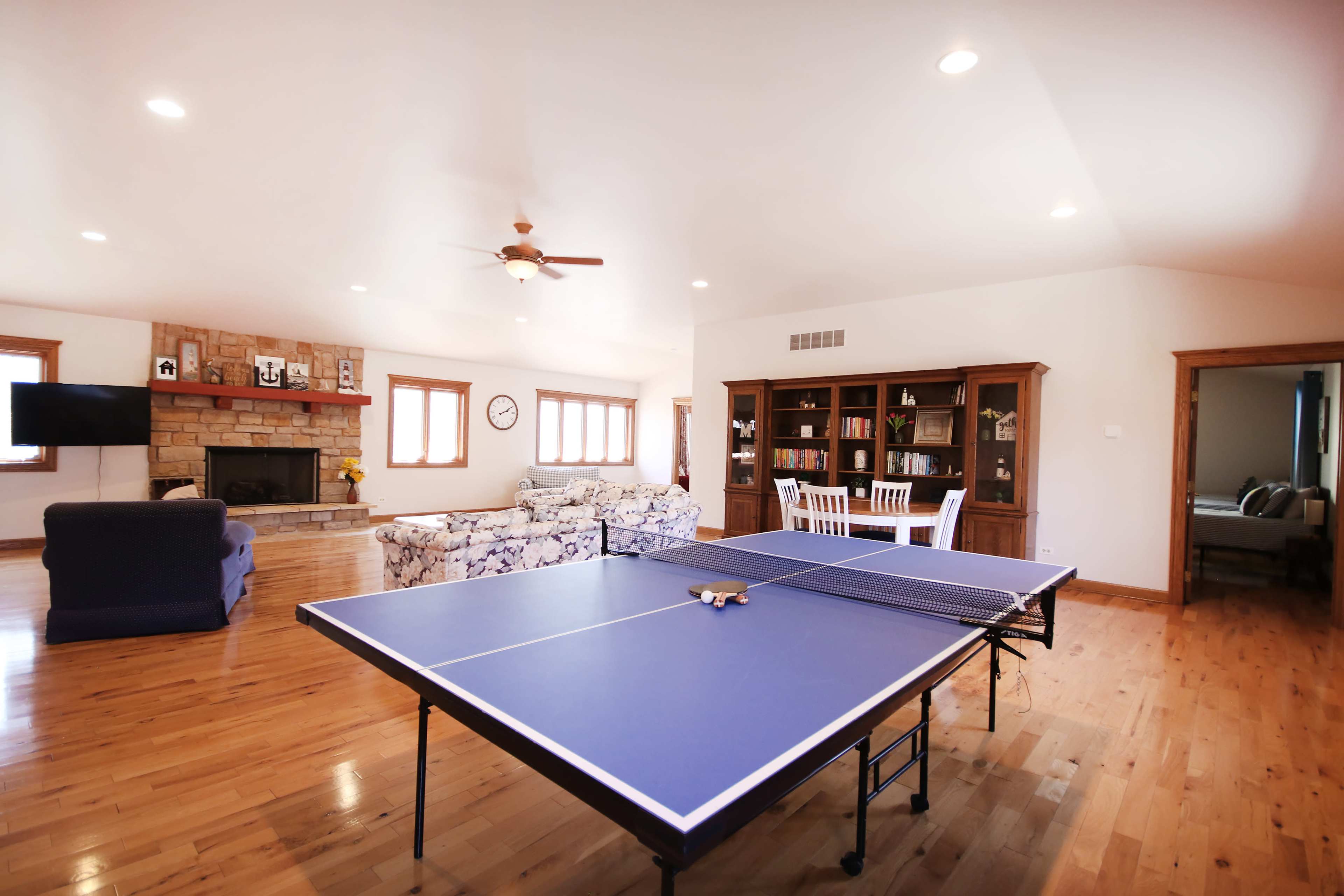 A spacious living area featuring a blue ping pong table, a stone fireplace, a television, and seating arrangements.
