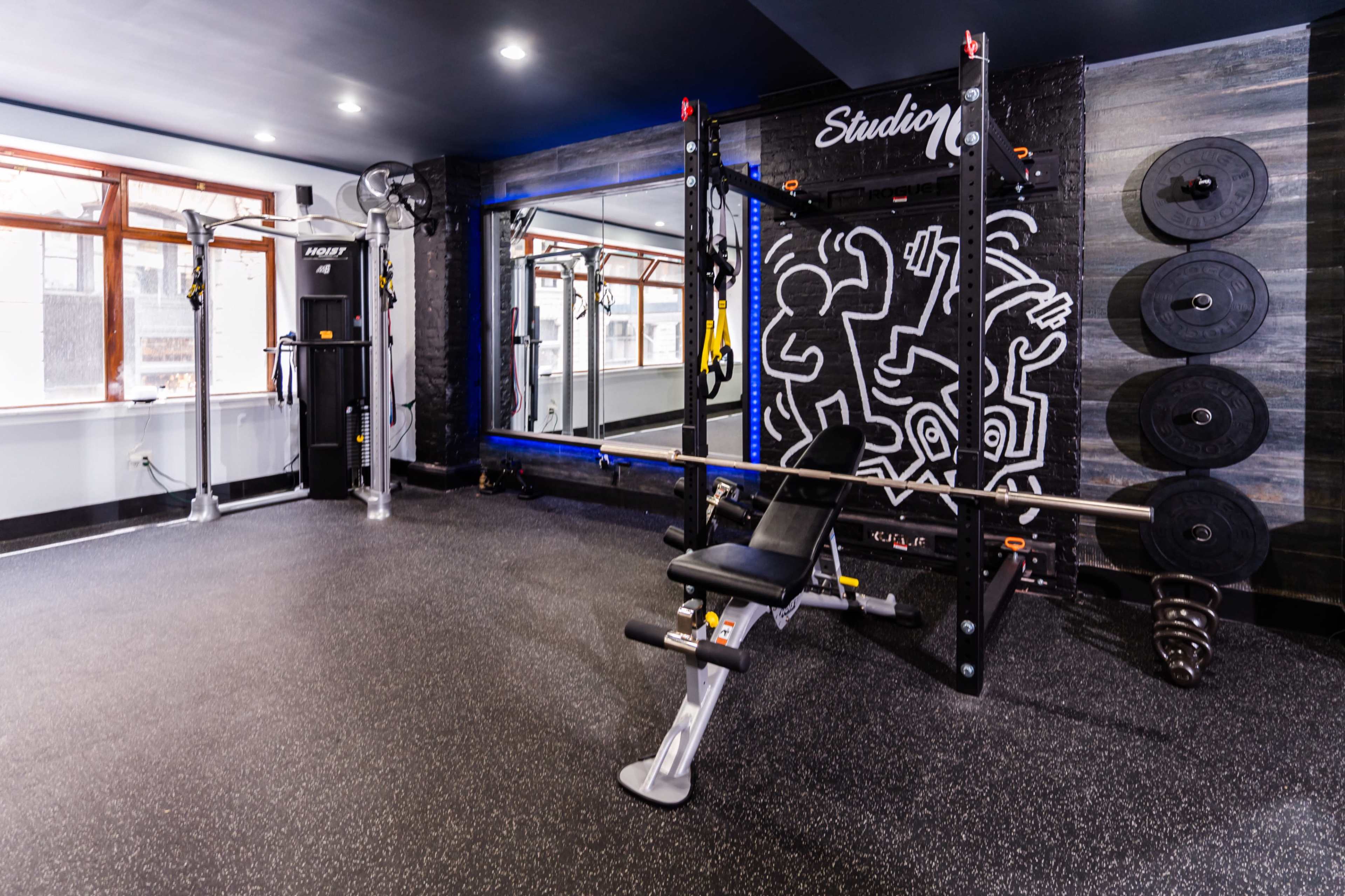 A well-equipped home gym featuring a weight bench, exercise machine, and free weights against a colorful wall with artwork.