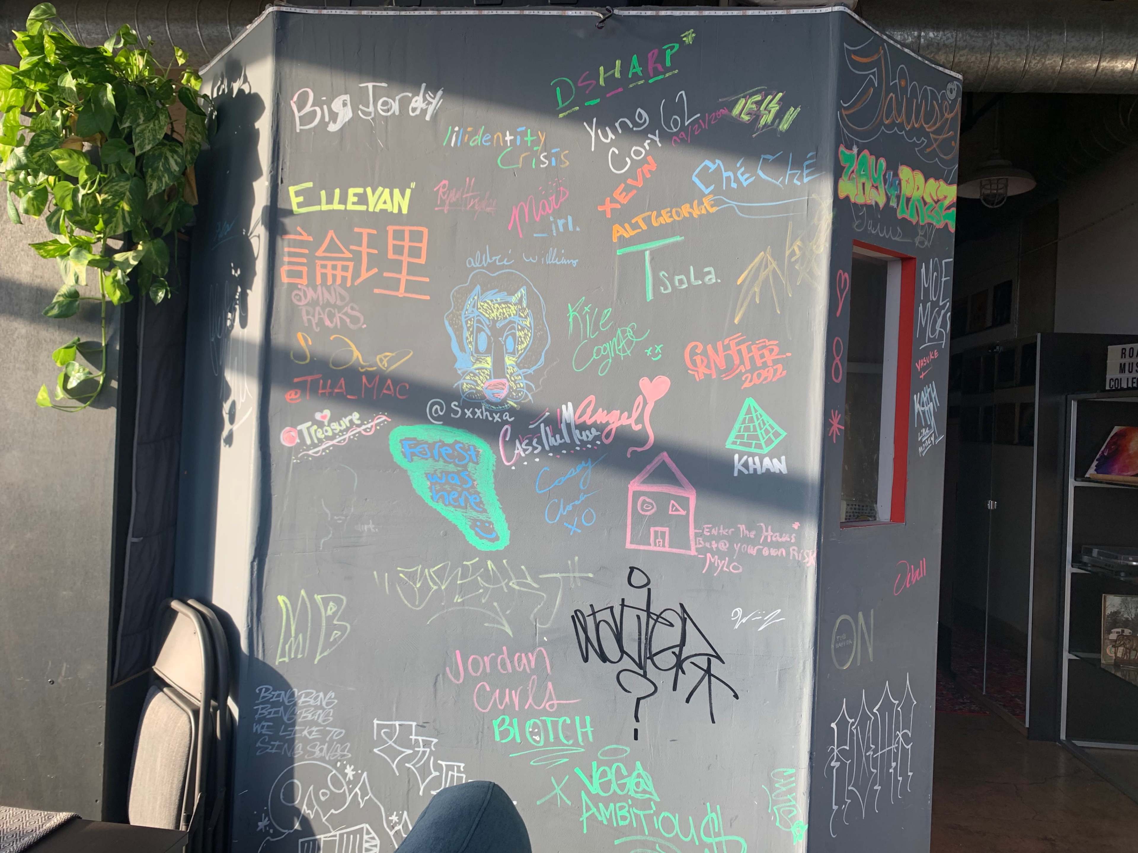 A wall covered with colorful graffiti and handwritten notes in a casual environment.