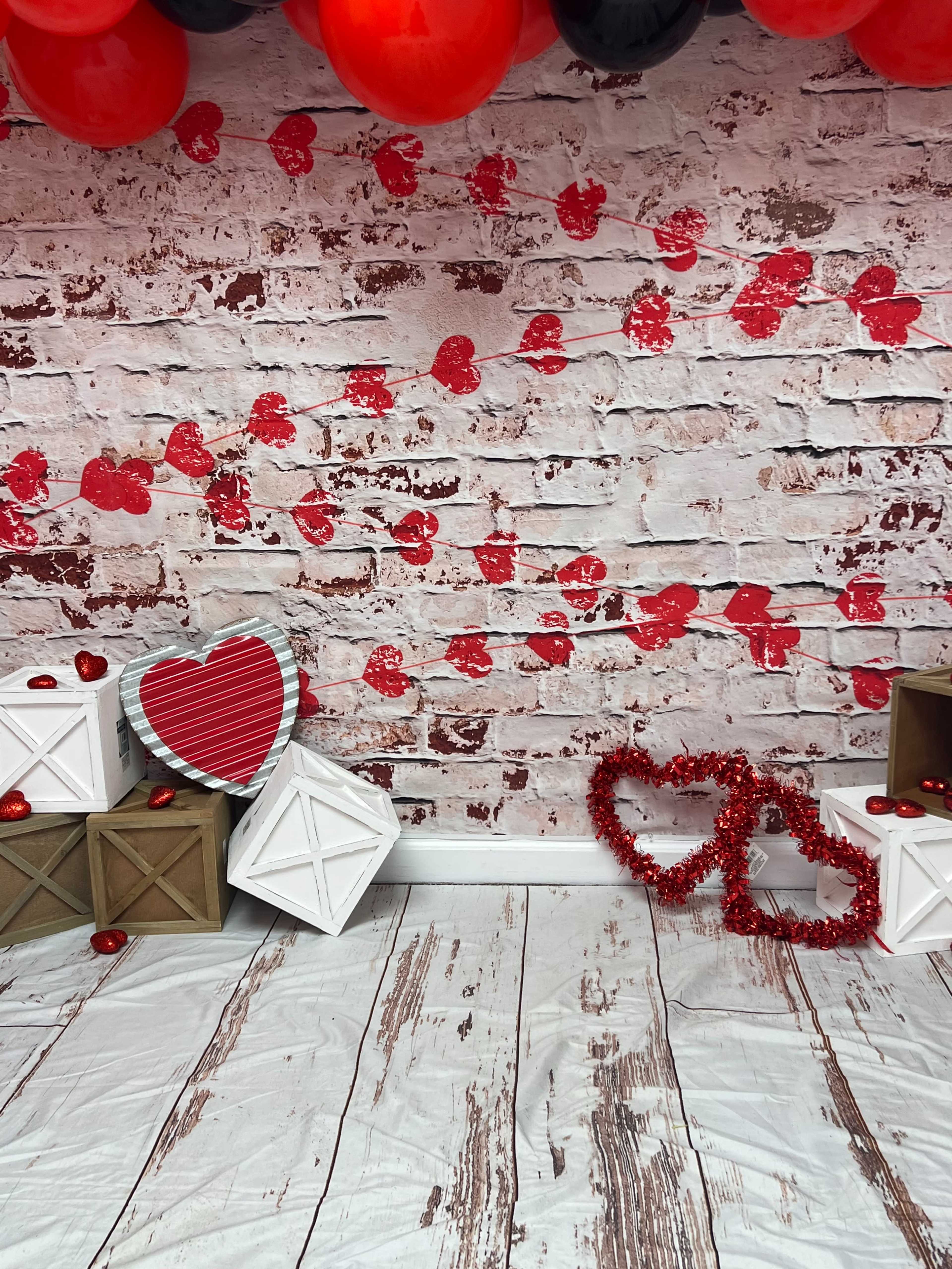 The scene features a backdrop of a brick wall decorated with red heart cutouts, alongside wooden boxes and a couple of heart-shaped decorations.