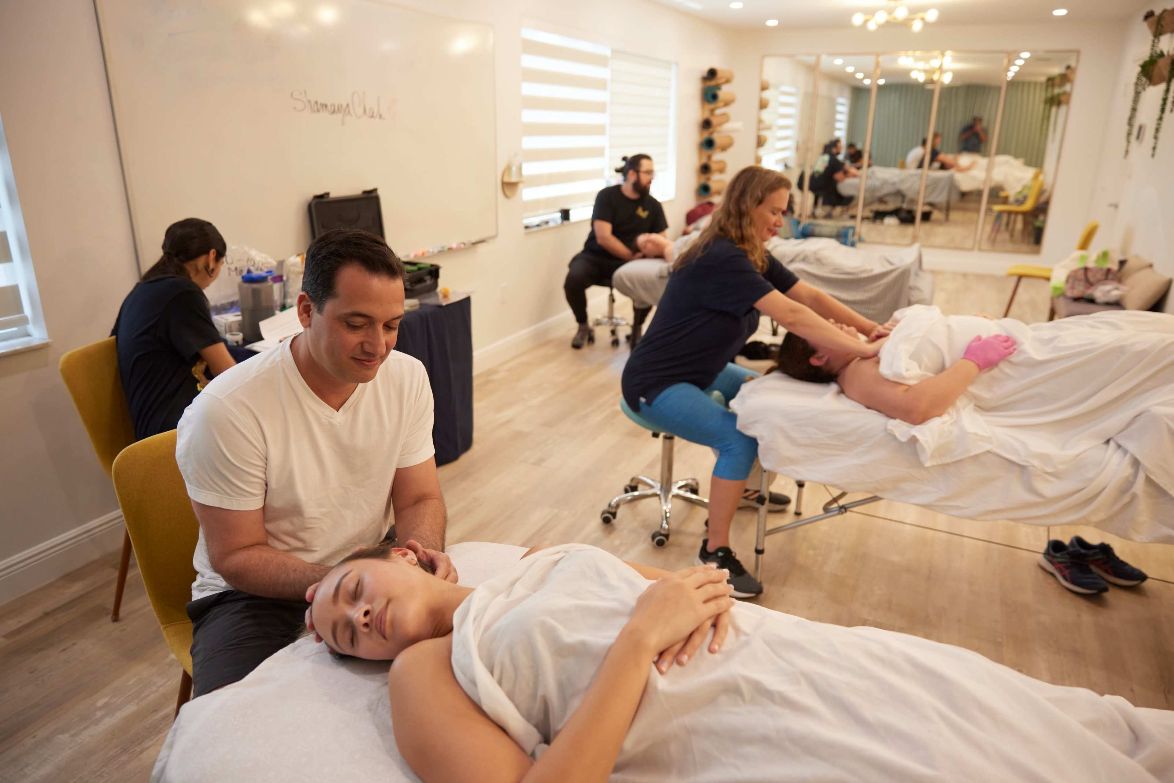 The image shows a wellness center where several people are receiving massages while others are engaged in related activities.
