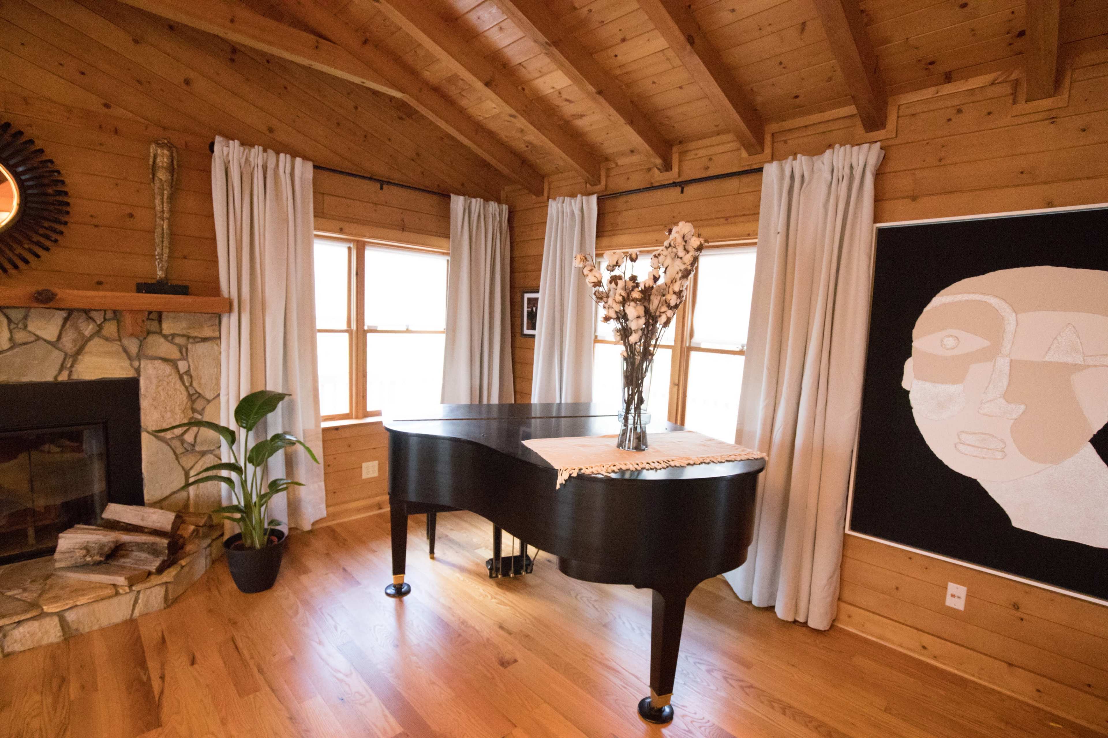 A grand piano is placed next to a stone fireplace in a room with wooden walls and large windows.