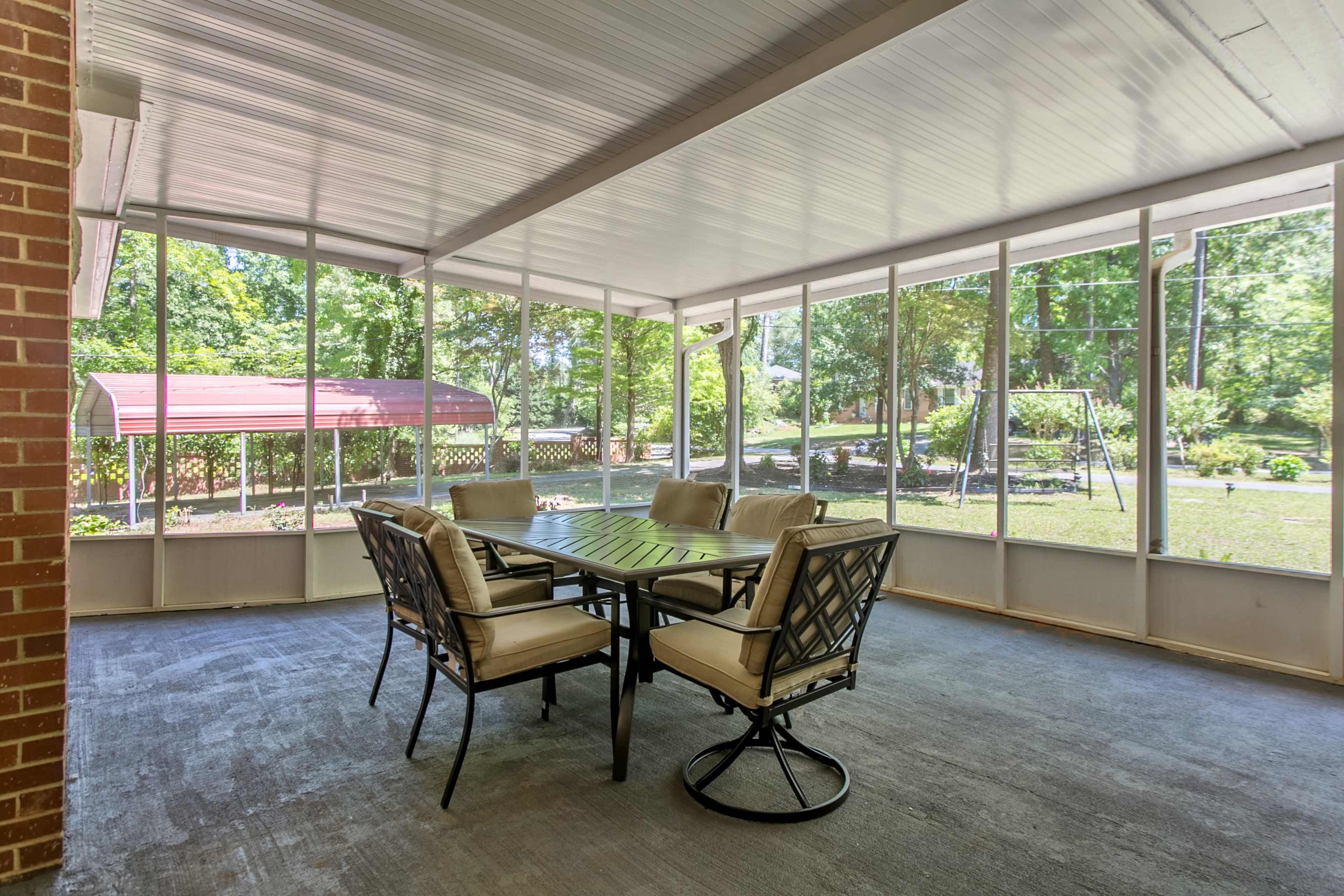 A screened-in porch with a dining table and chairs, surrounded by trees and a backyard view.