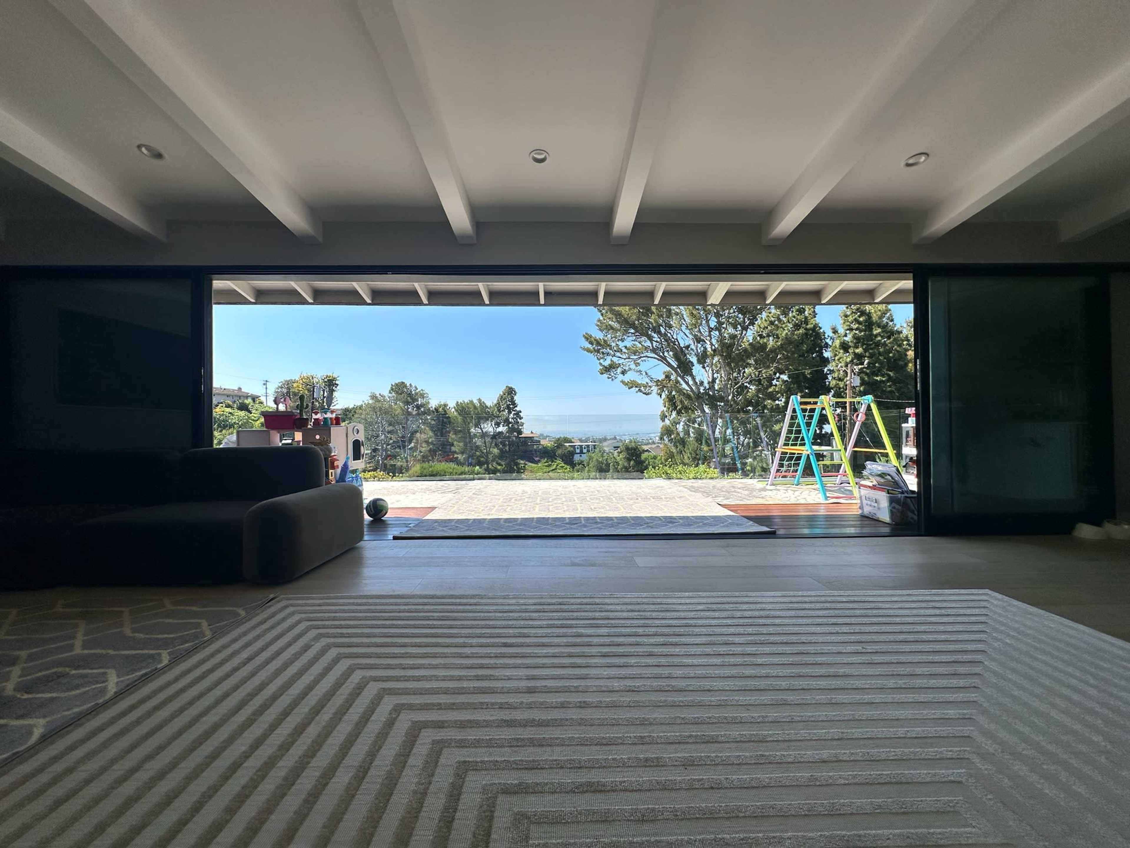 An open interior space with a large glass door leading to an outdoor area, framed by trees and a view of the horizon.