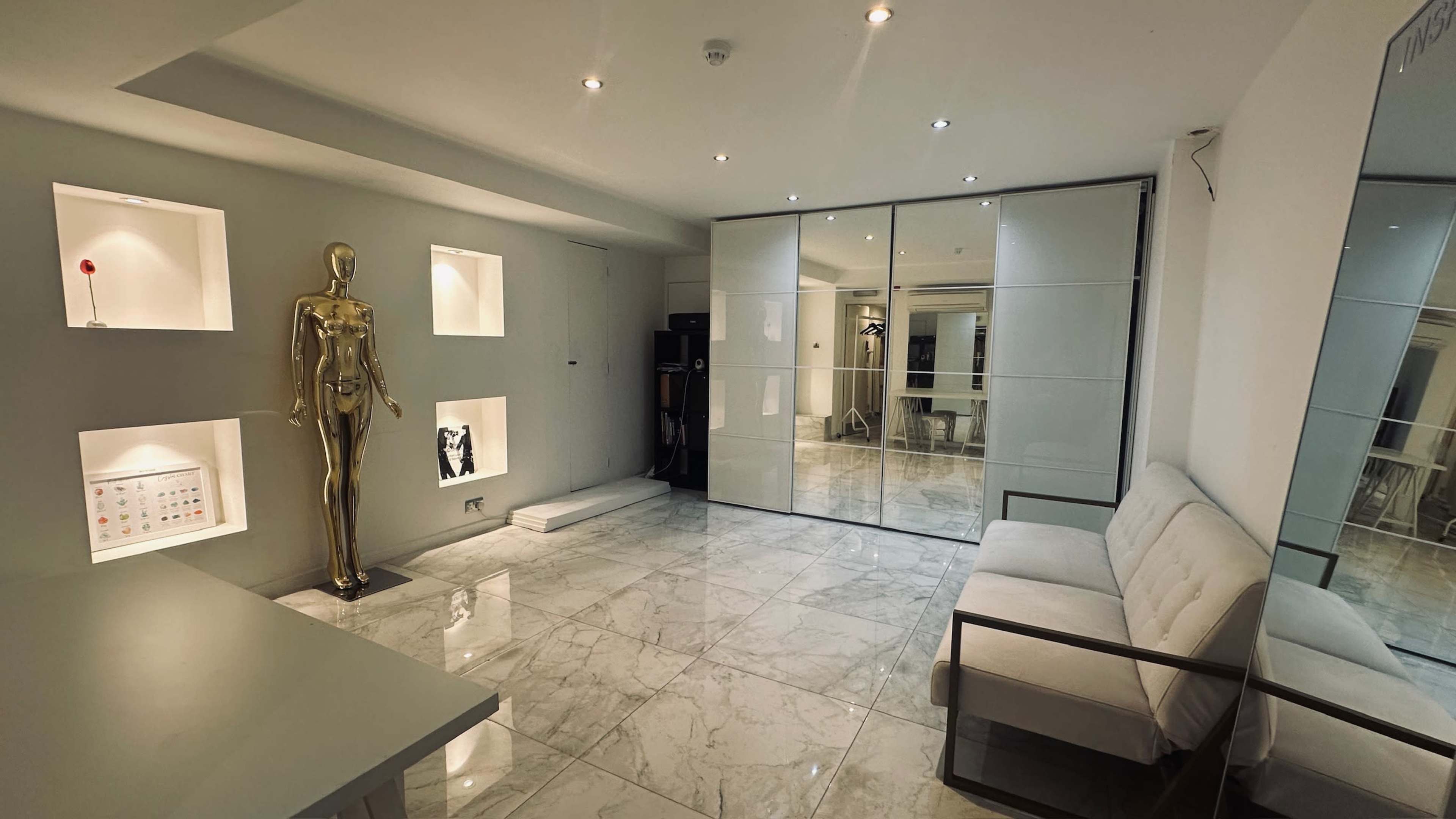 The image shows a modern interior space featuring a gold mannequin, marble flooring, and sliding glass doors.