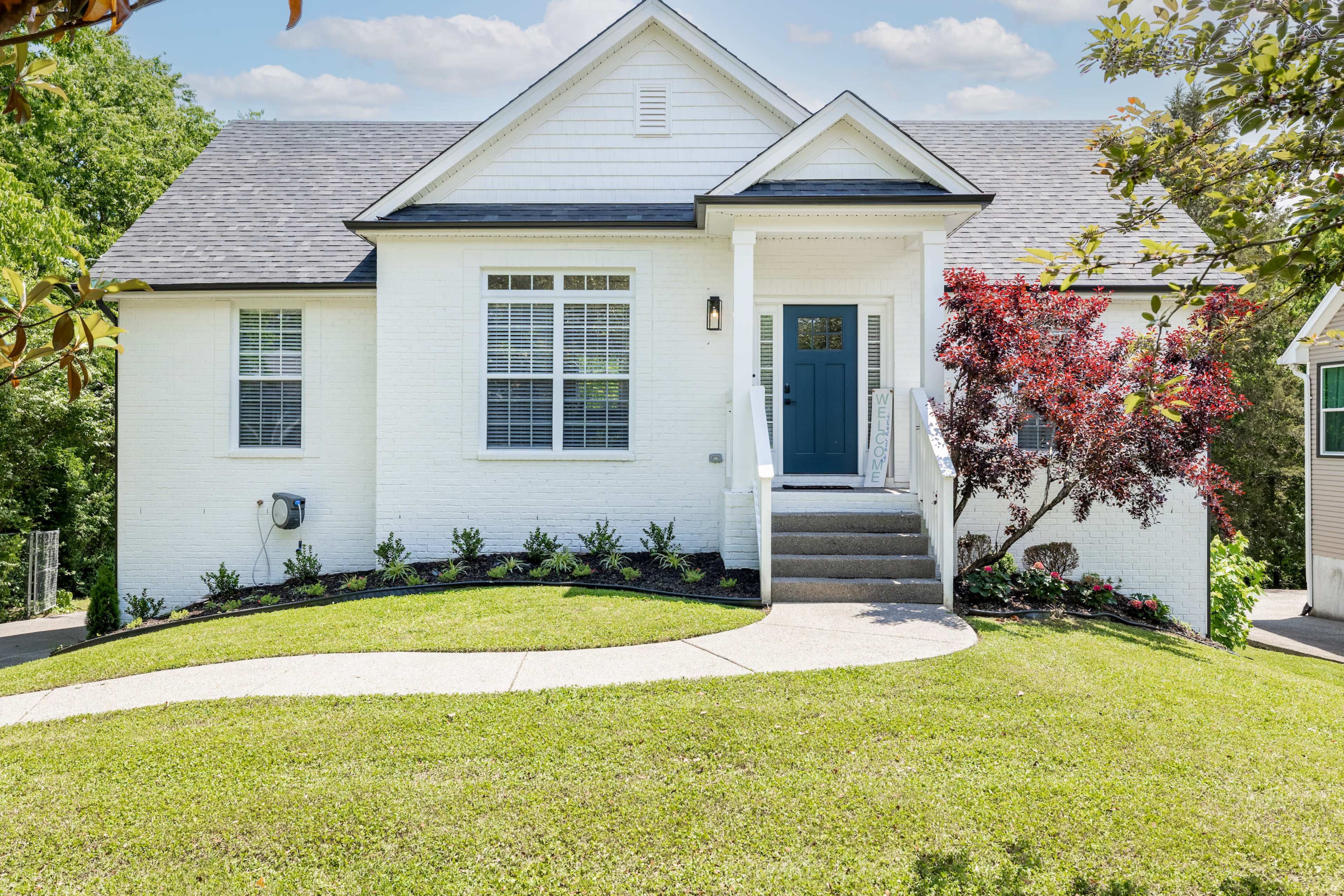A single-story white house with a blue front door, surrounded by manicured landscaping and stone steps leading to the entrance.