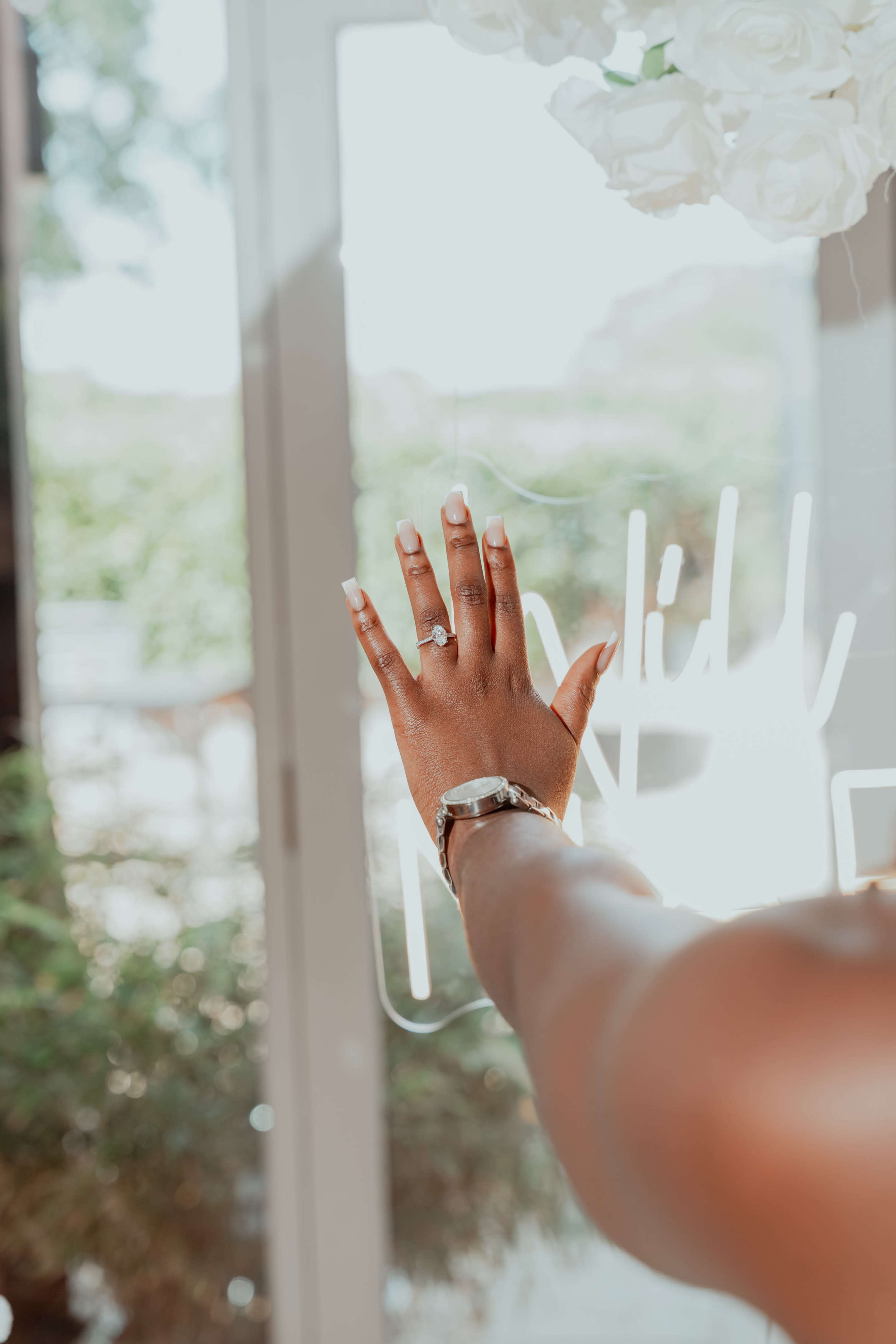 A hand adorned with a ring reaches towards a glass door featuring decorative white lettering.