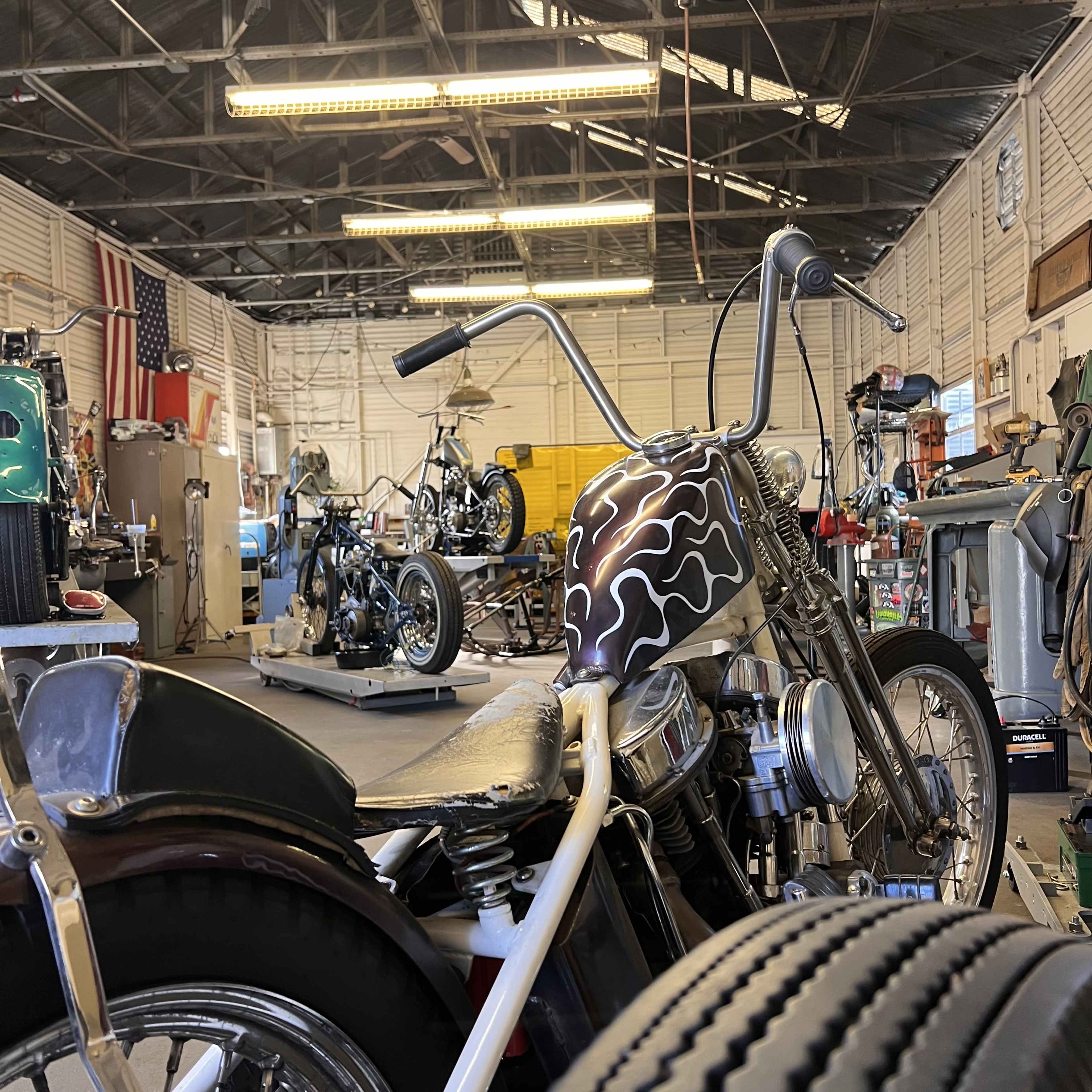 The image shows a motorcycle shop with several bikes displayed and workshop tools scattered around.