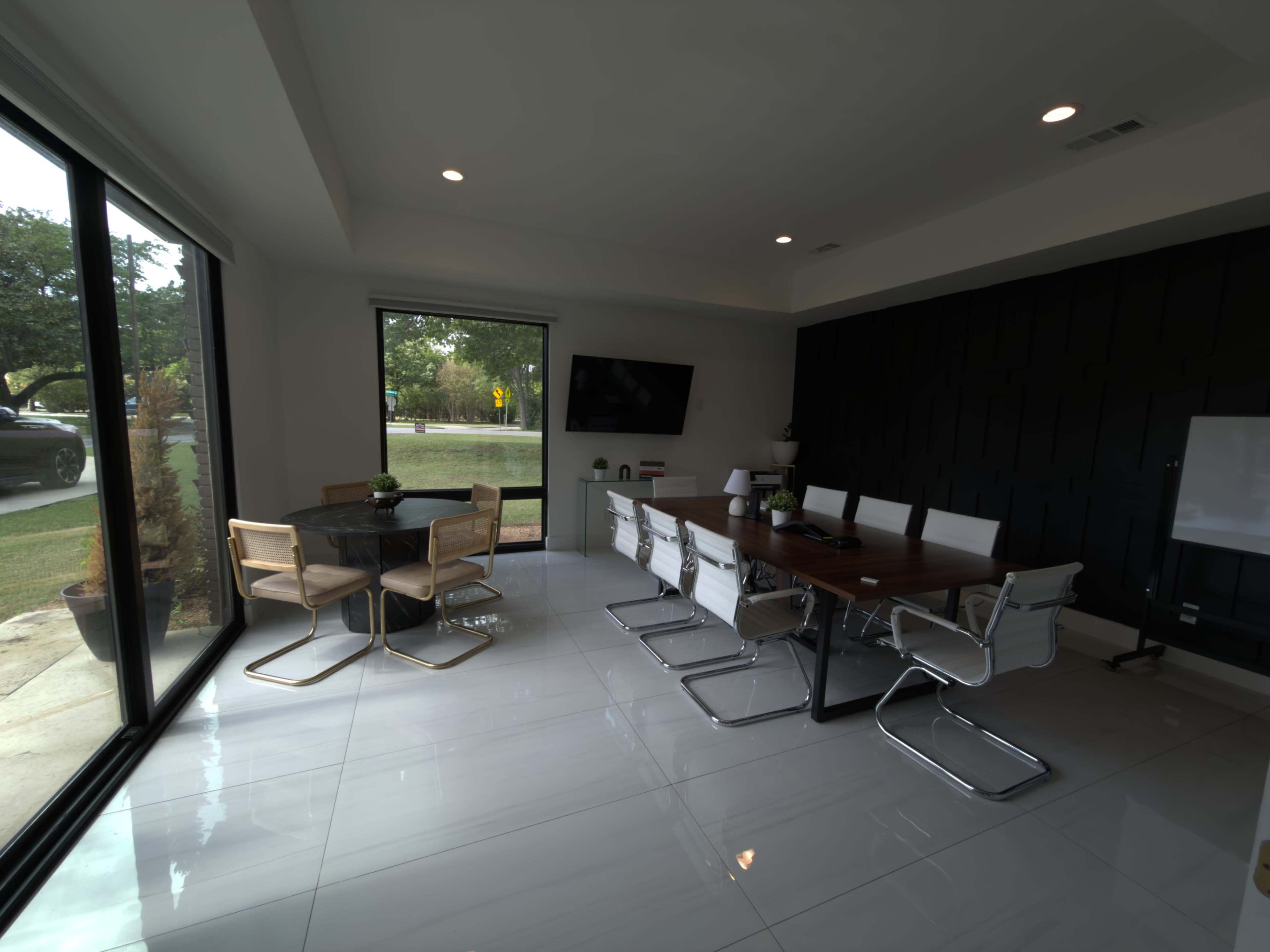The image shows a modern conference room with a long wooden table, white chairs, and large windows providing natural light.