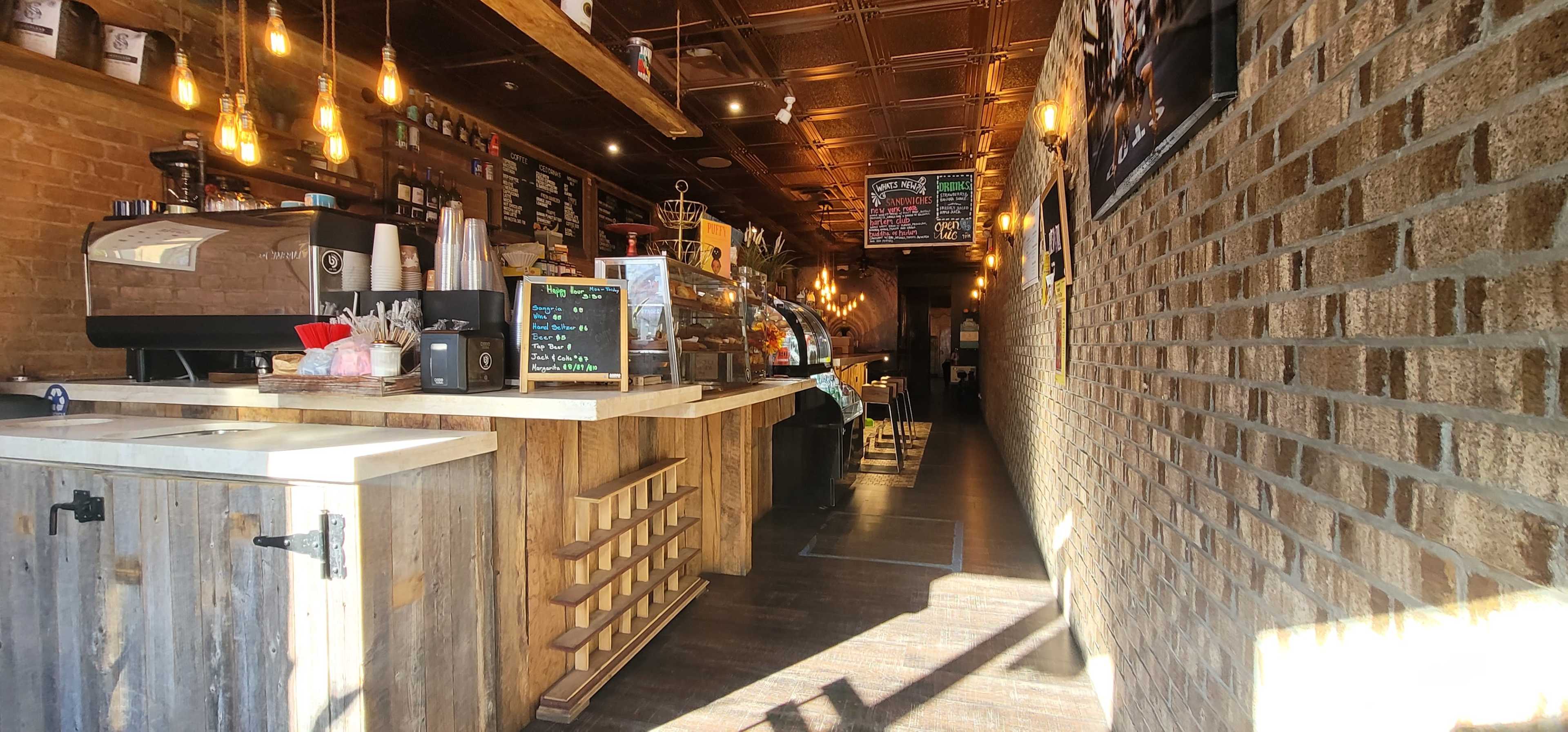 The interior of a coffee shop featuring a wooden counter, shelves with products, and illuminated seating along a narrow corridor.