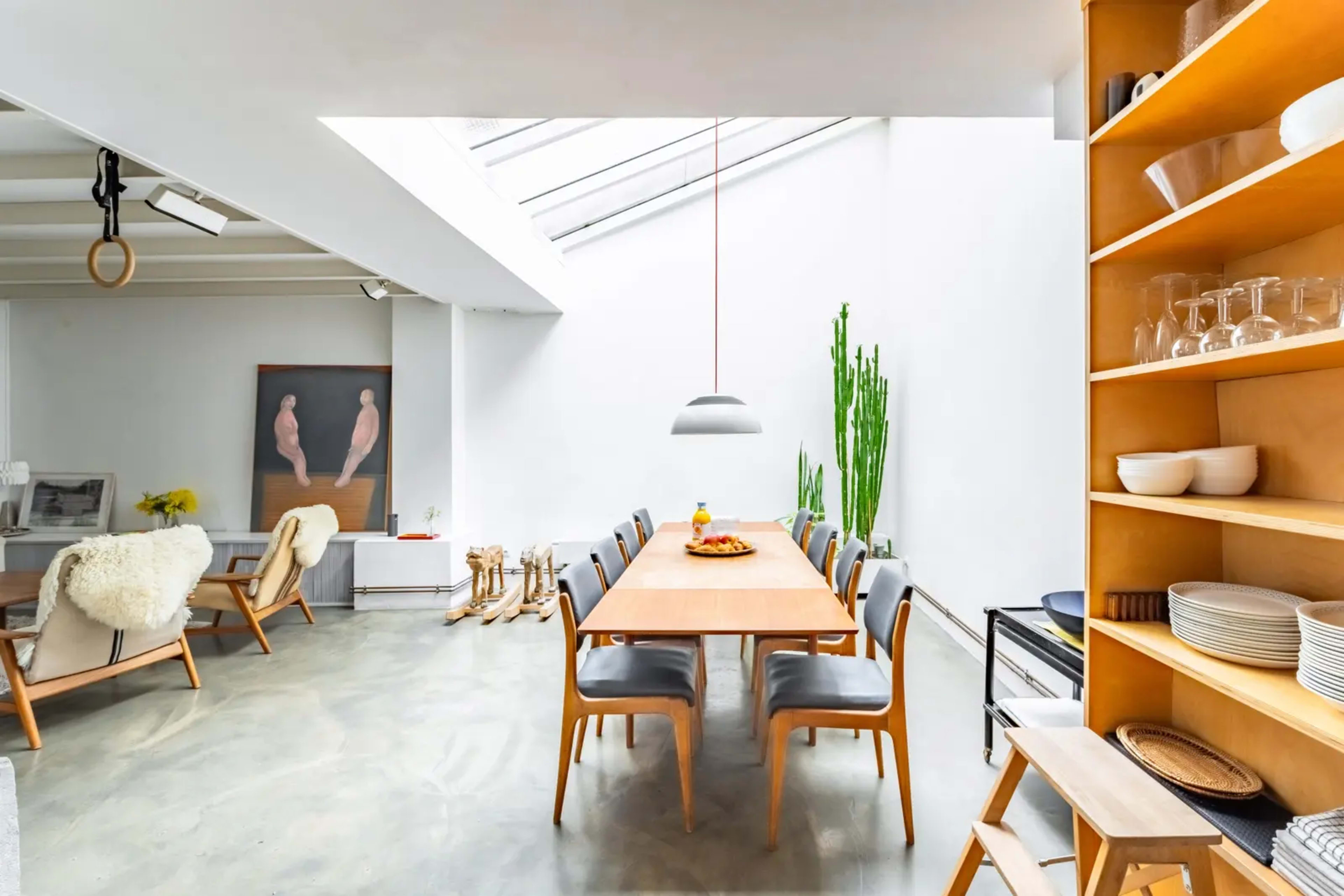 A modern dining area features a wooden table surrounded by gray chairs, with a large window allowing natural light to illuminate the space.