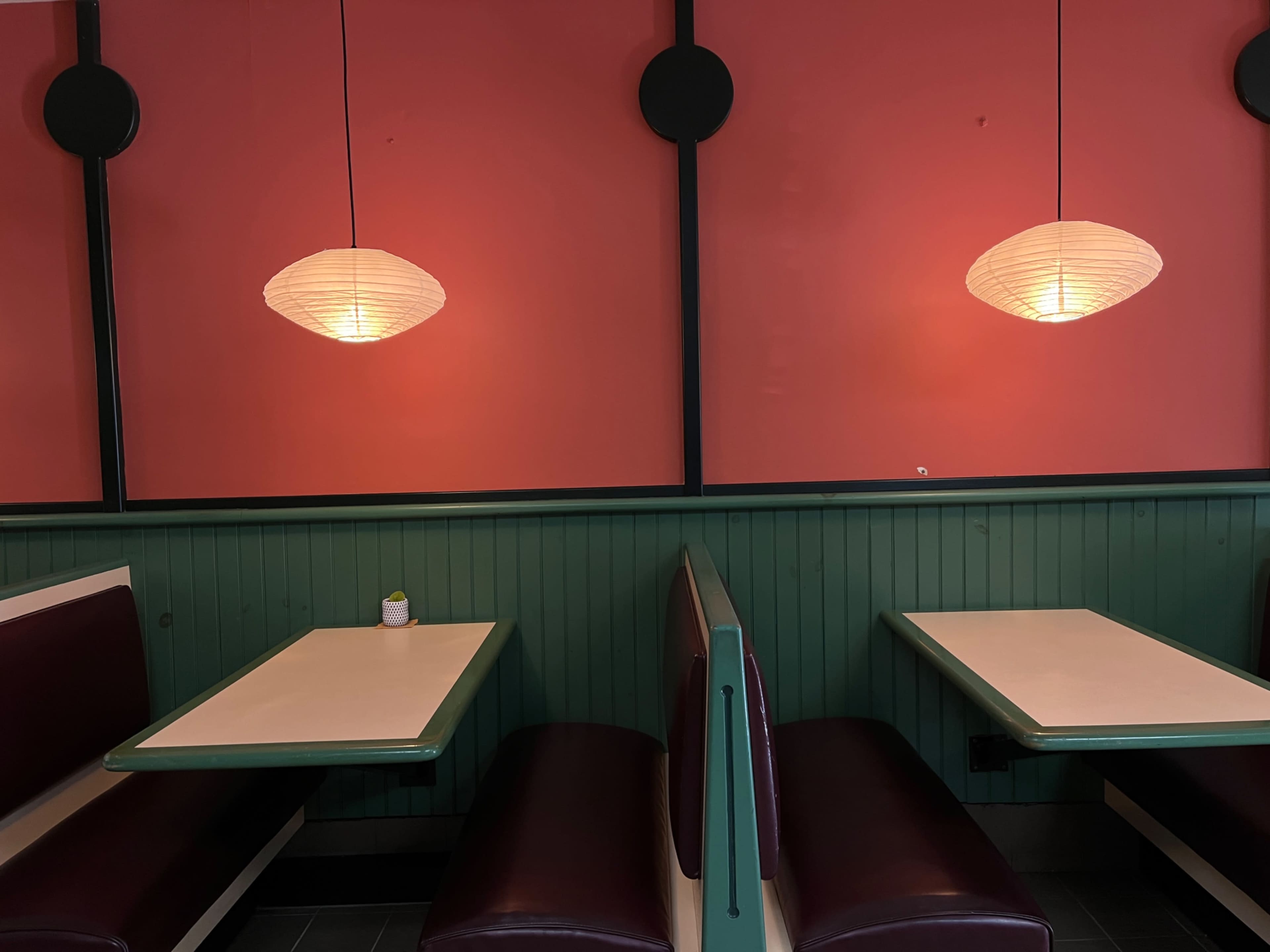 A diner-style interior with two booths facing each other, separated by light fixtures hanging from the ceiling against a pink wall.
