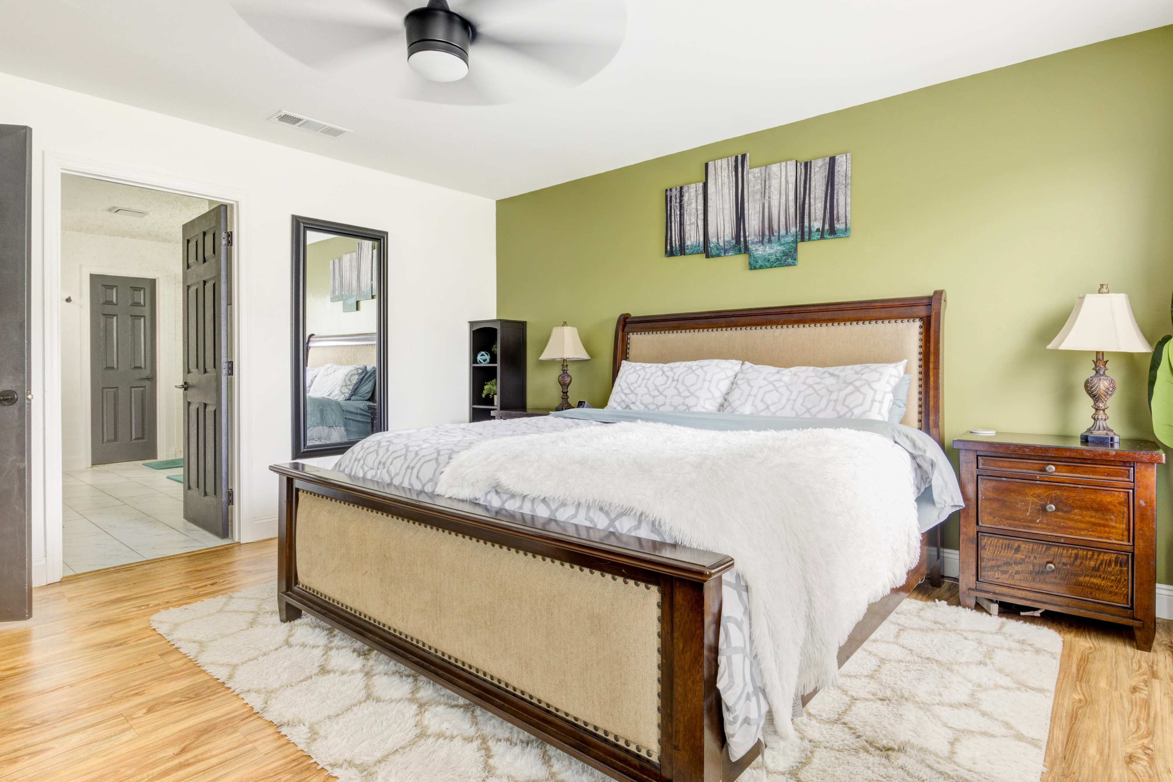 A well-decorated bedroom featuring a wooden bed frame, a green accent wall, and a plush rug on a hardwood floor.