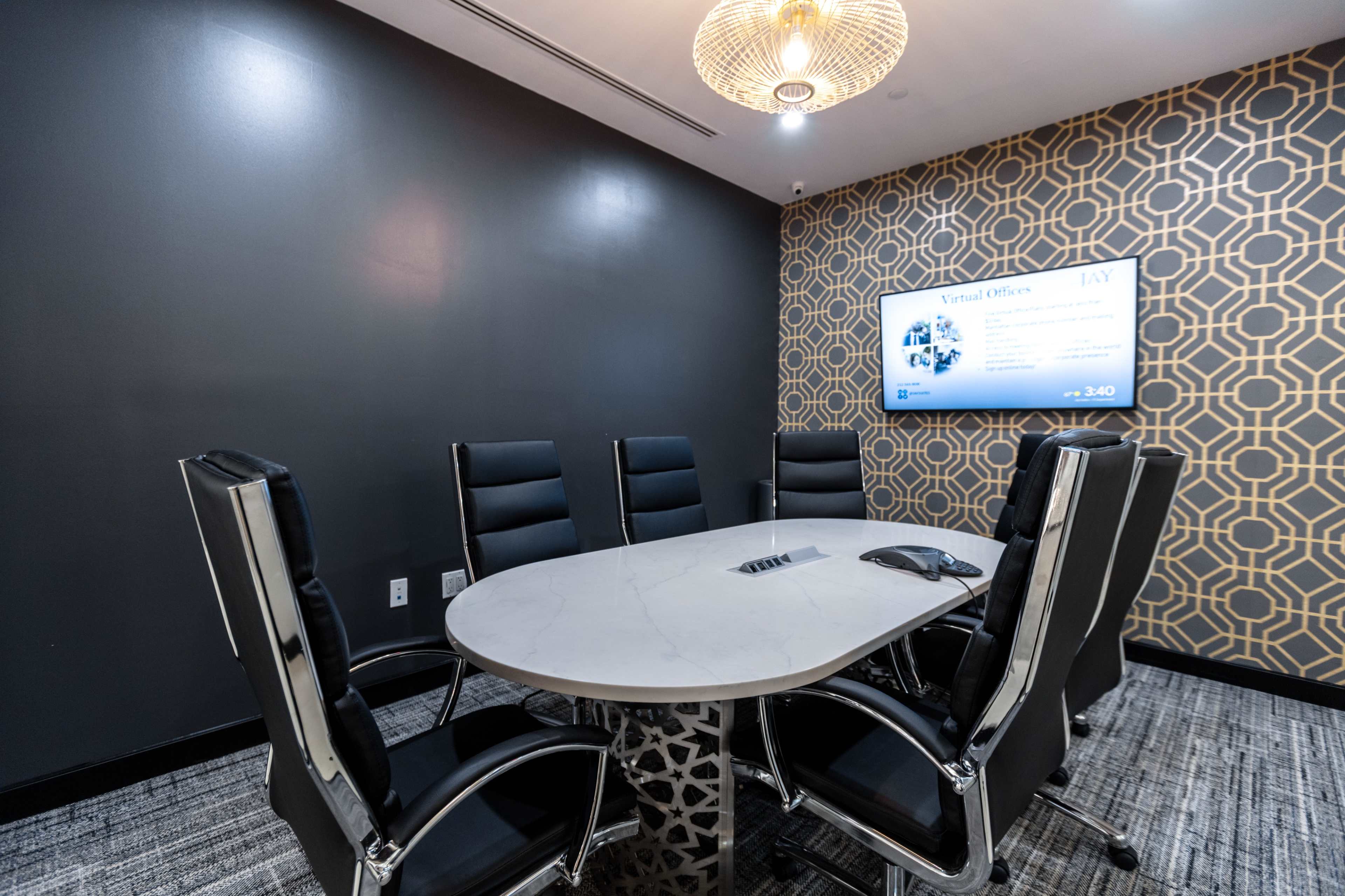 A modern conference room features a round table surrounded by black leather chairs, with a large screen displaying information on a patterned wall.