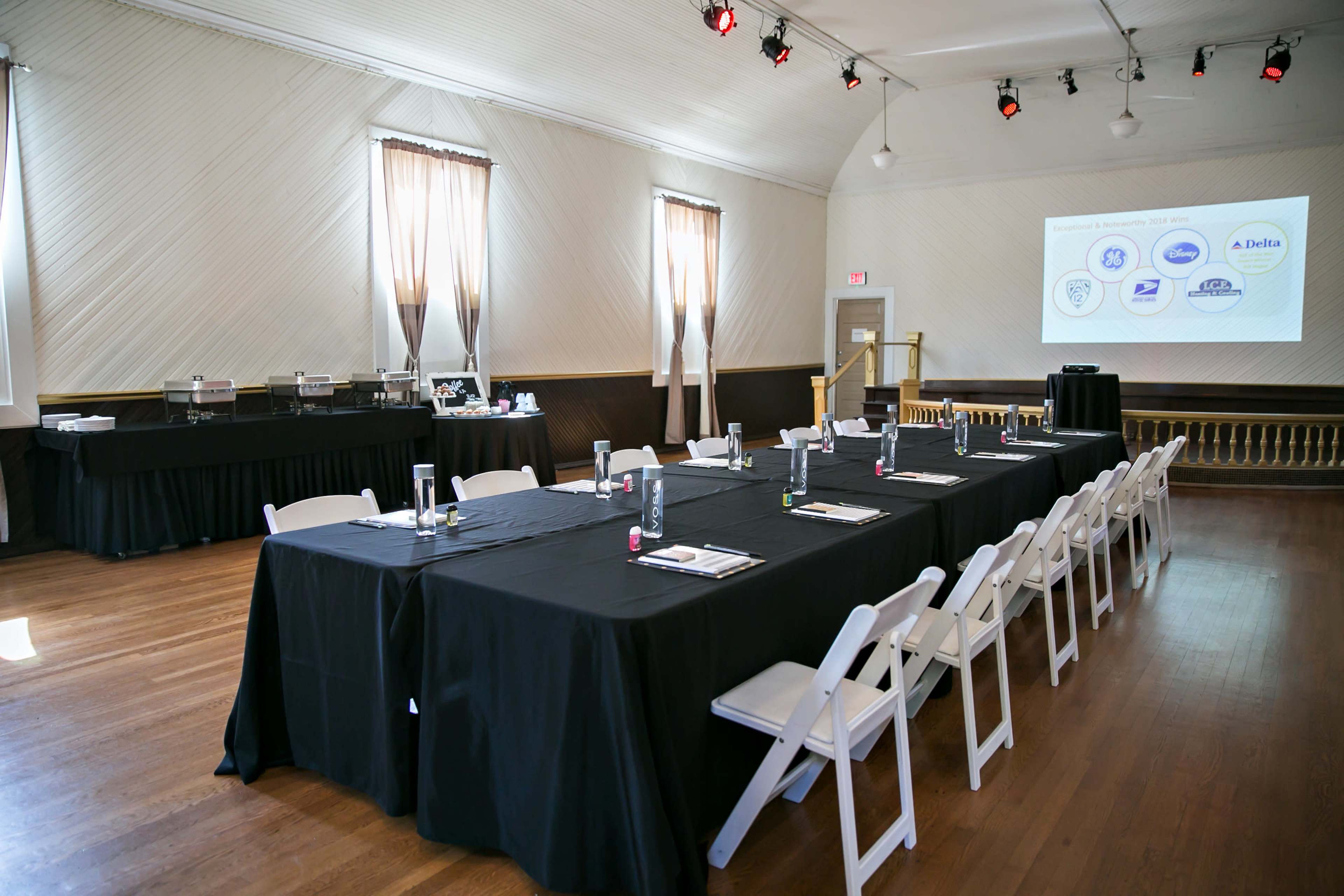 A conference room is set up with black tablecloths covering long tables and a projector screen displaying logos at one end.