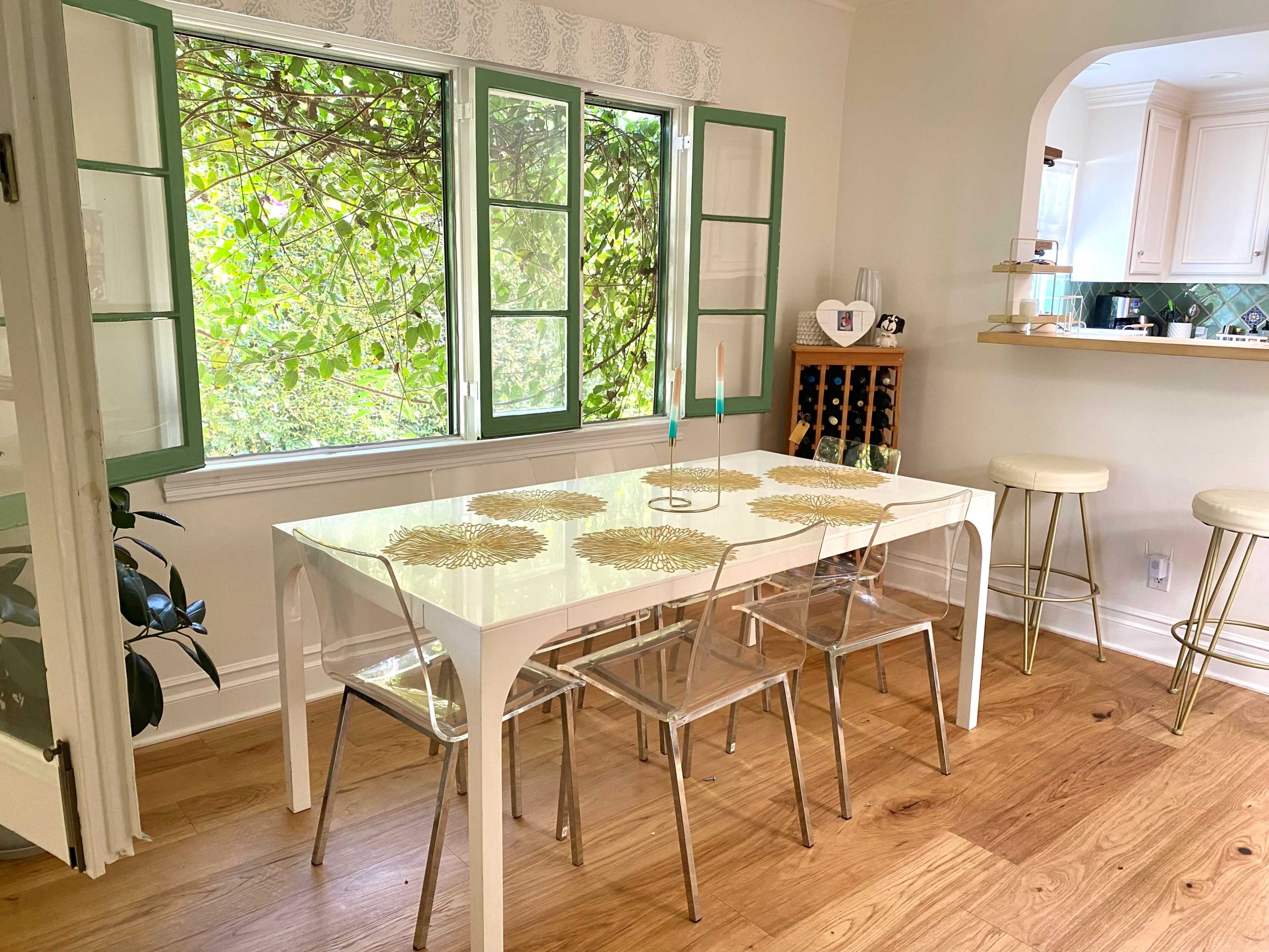 A modern dining area features a clear acrylic table surrounded by transparent chairs, with large windows allowing natural light to fill the space.