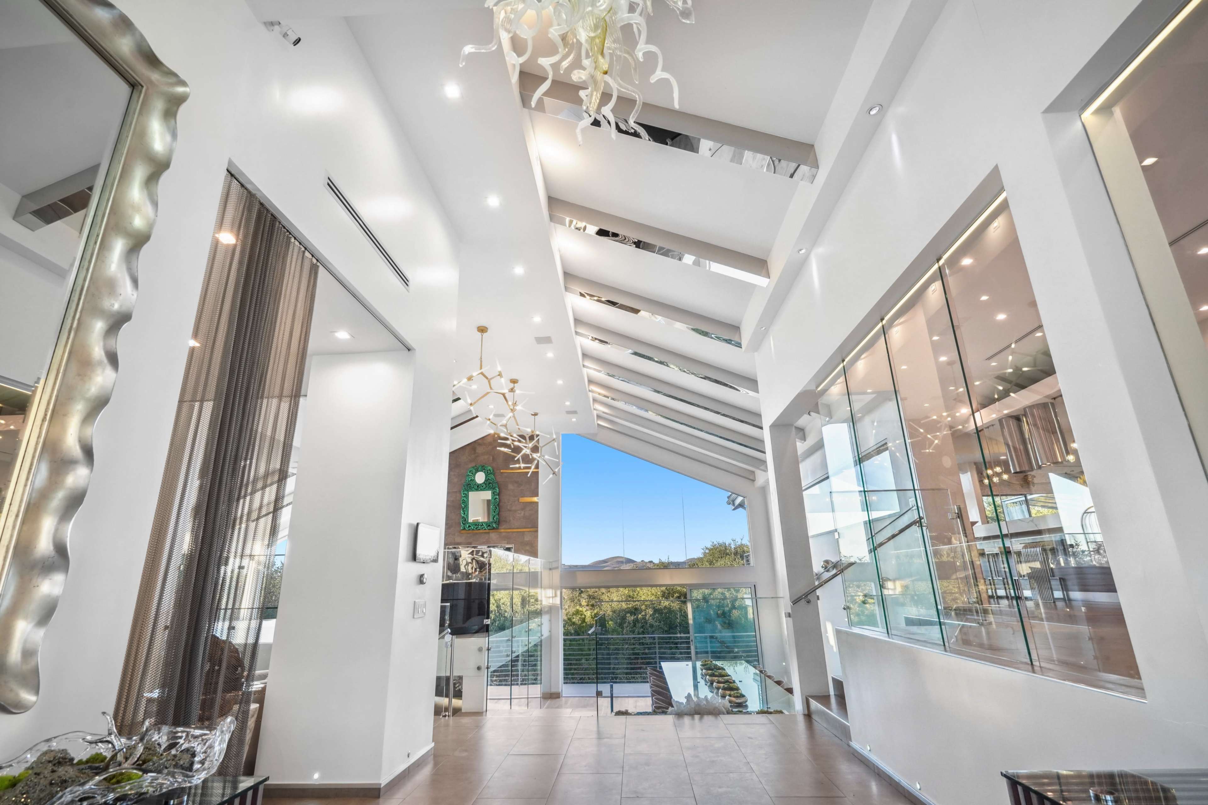 The image shows a modern interior space with high ceilings, large glass windows, and contemporary lighting fixtures.