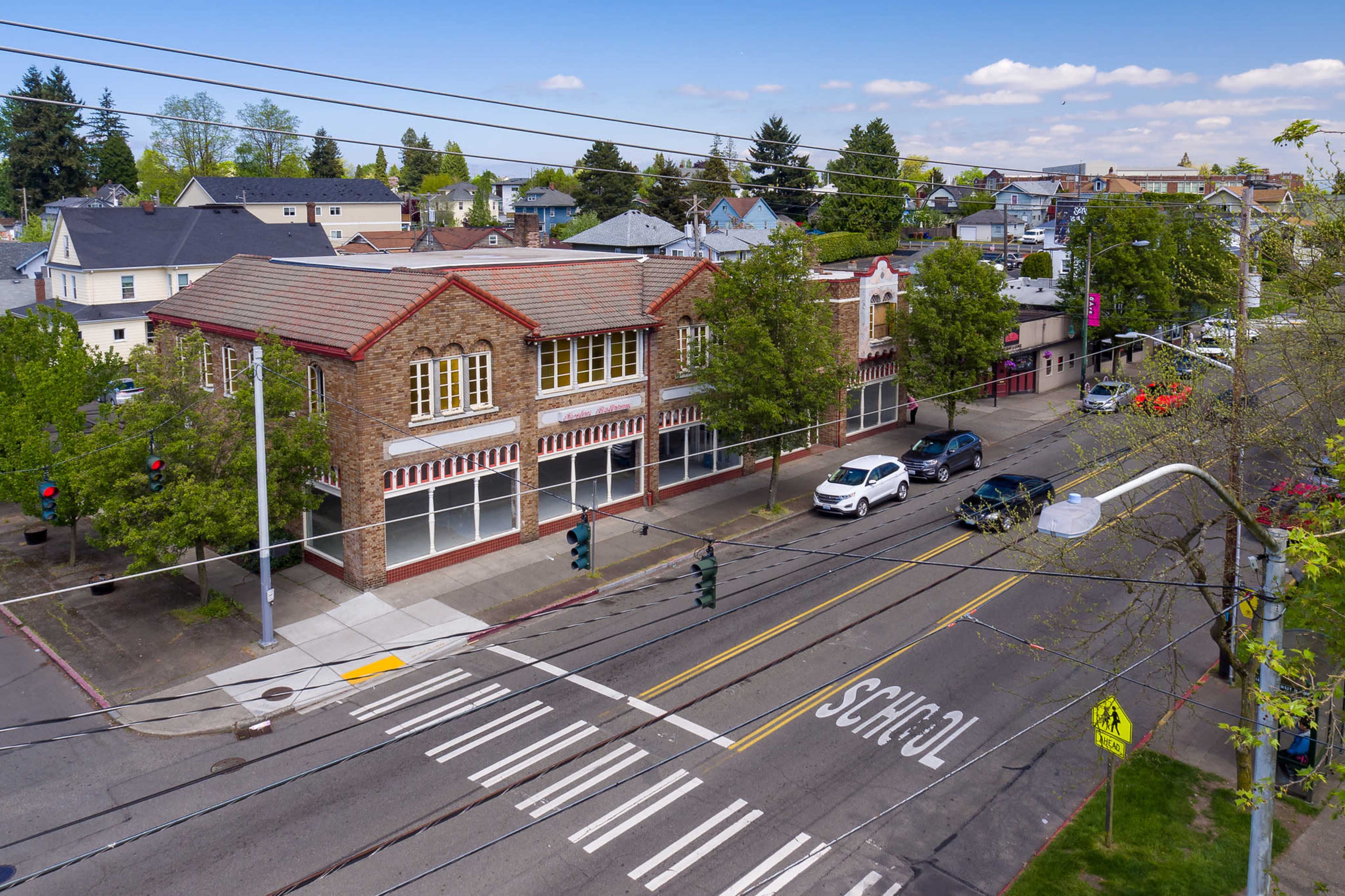 A street corner with a brick building housing retail spaces, traffic lights, and a crosswalk marked "SCHOOL."