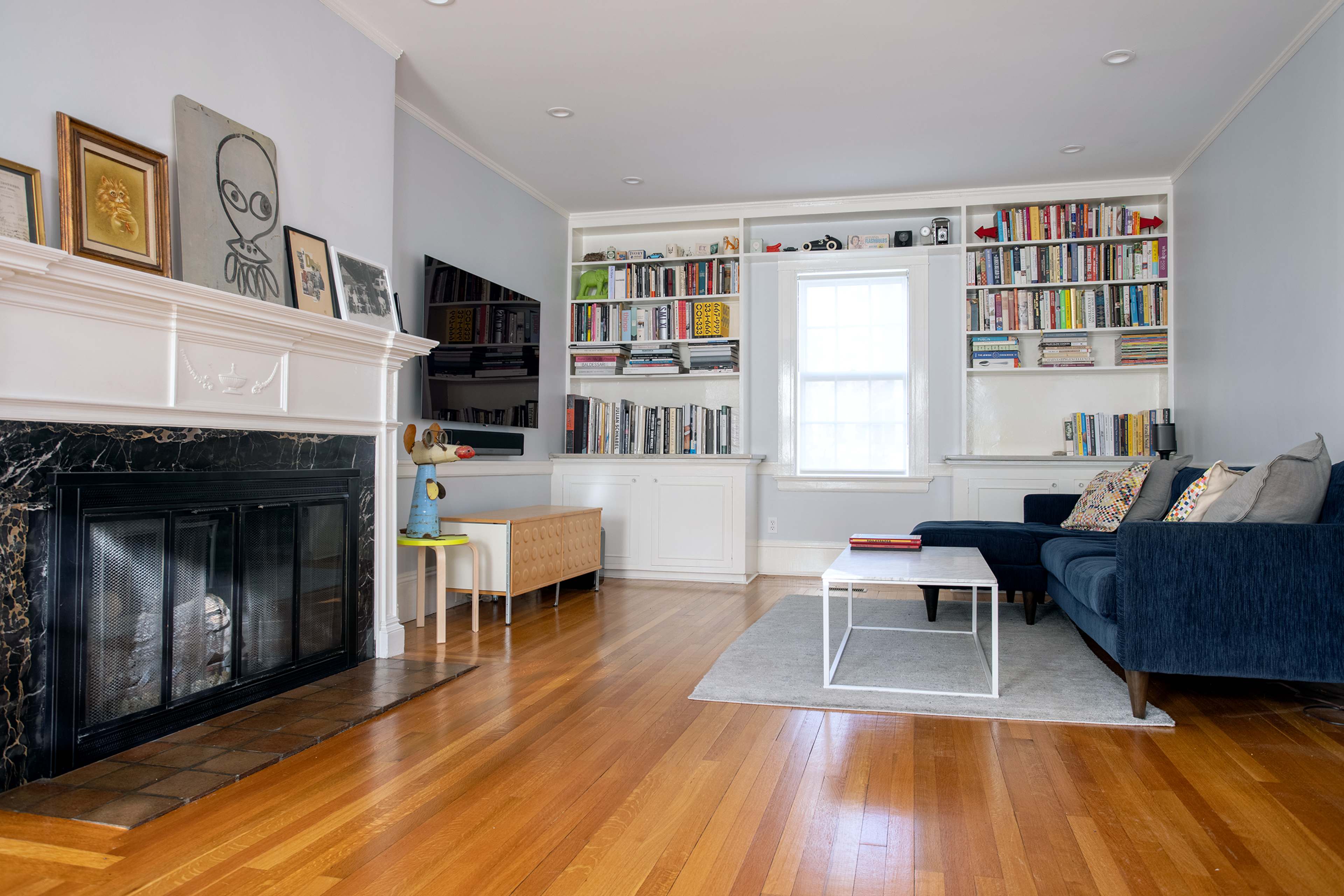 A modern living room featuring a fireplace, built-in bookshelves filled with books, and a blue sofa arranged with a coffee table on a light rug.