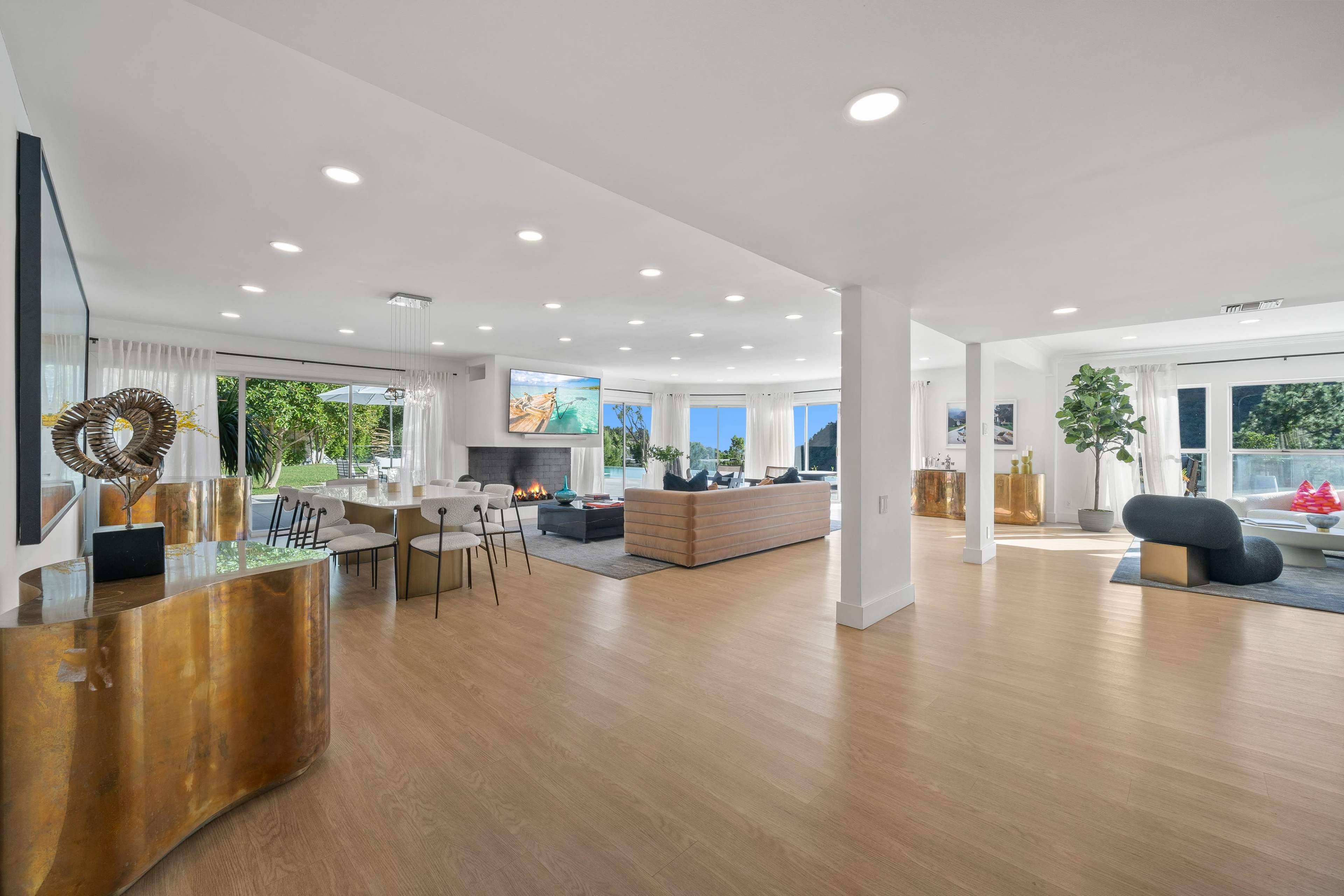 A modern, open-concept living space featuring a mix of dining and lounging areas with large windows that provide natural light and views of the outdoors.