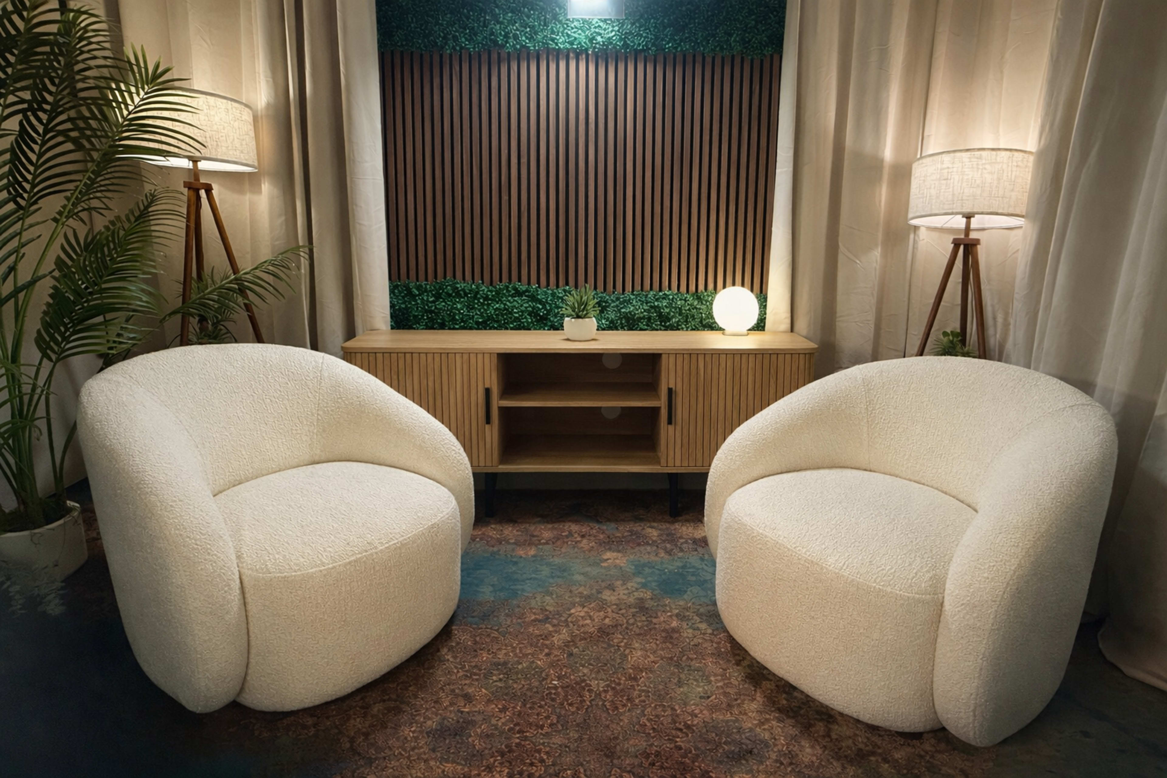 The image shows two round, white chairs positioned opposite each other in a room featuring a wooden console and a decorative green backdrop.
