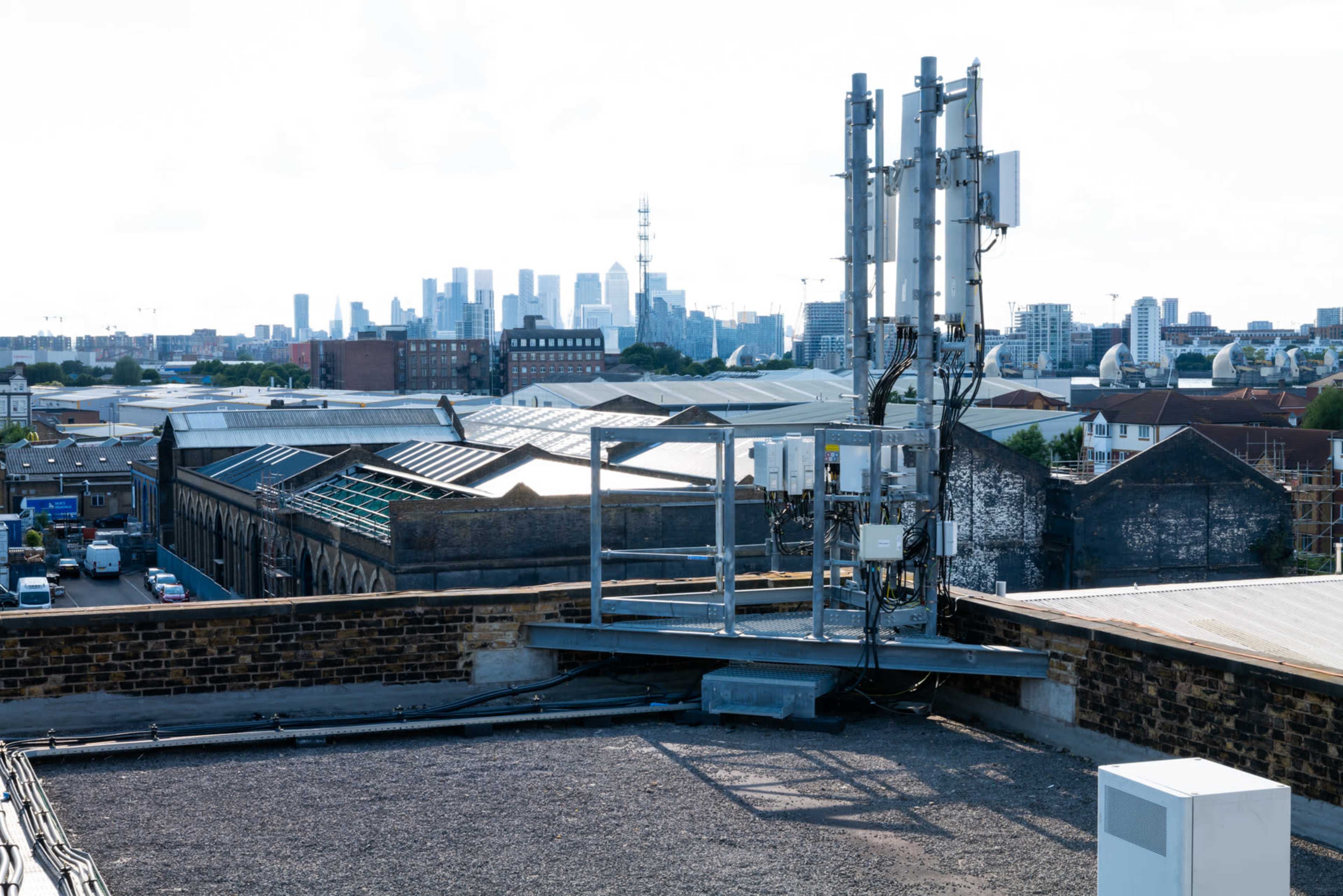A rooftop with telecommunications equipment overlooks a city skyline featuring tall buildings and a television tower in the distance.