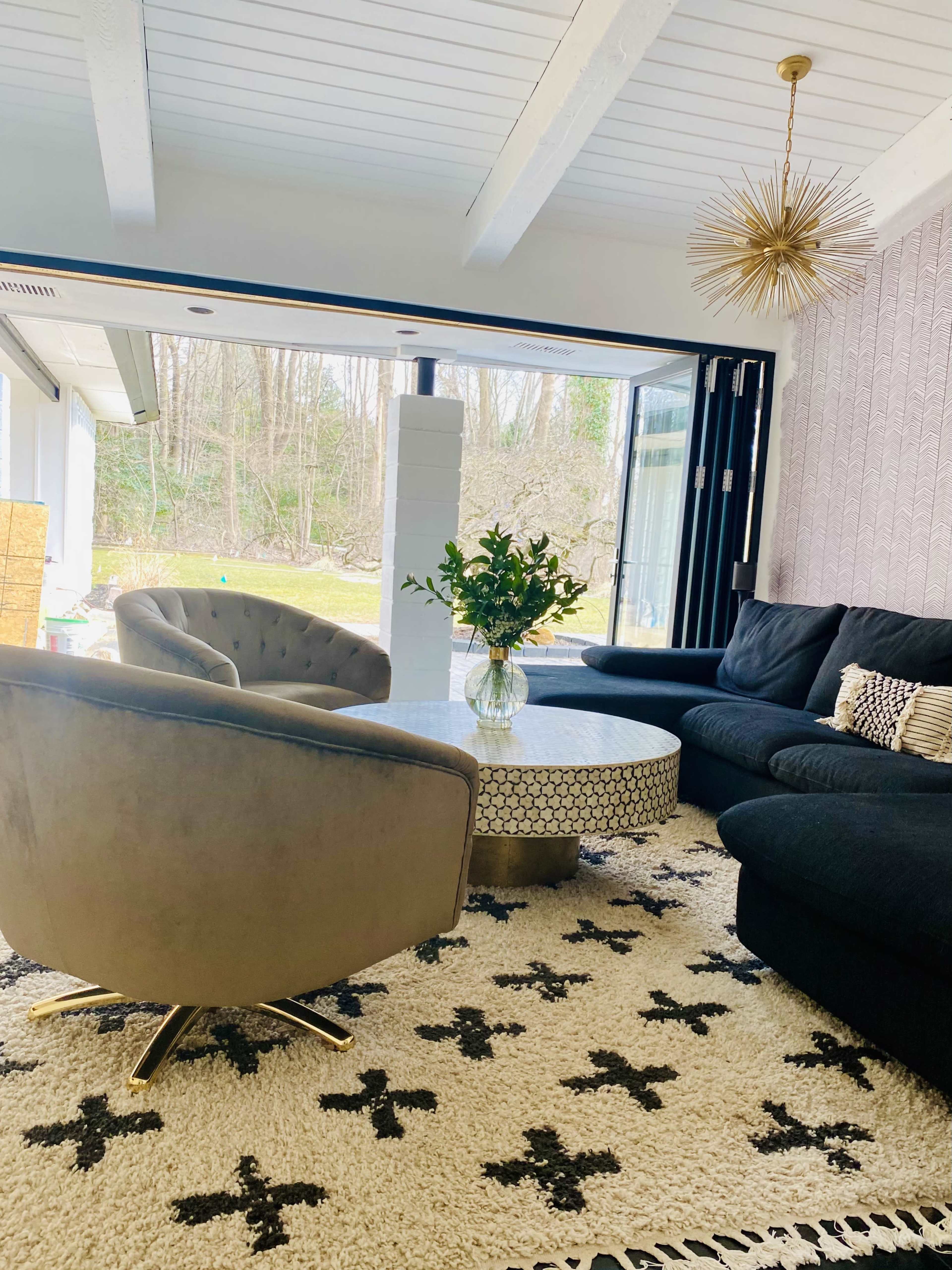 The living room features a circular coffee table surrounded by a dark sofa and two accent chairs, with a large window overlooking a green landscape.