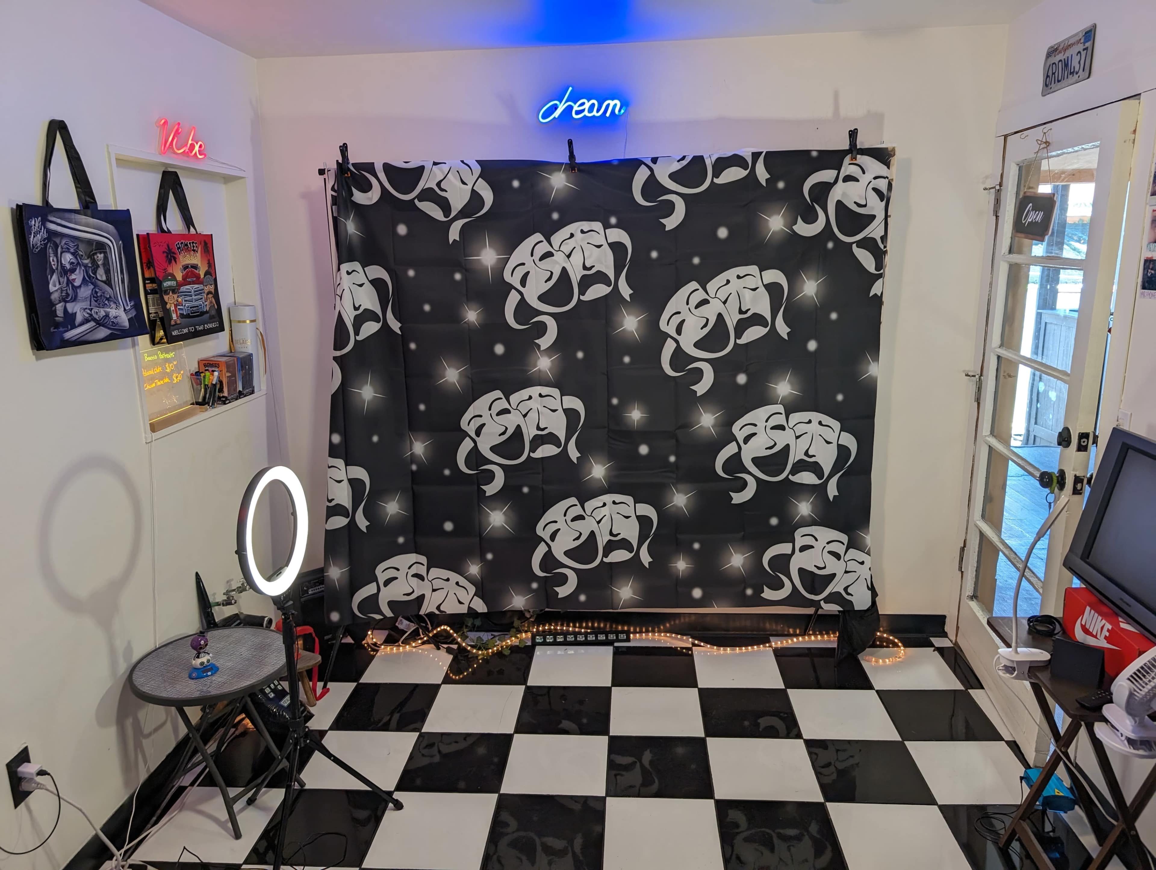 A small room with a black and white checkered floor, featuring a backdrop with theater masks, a circular light, and a table.