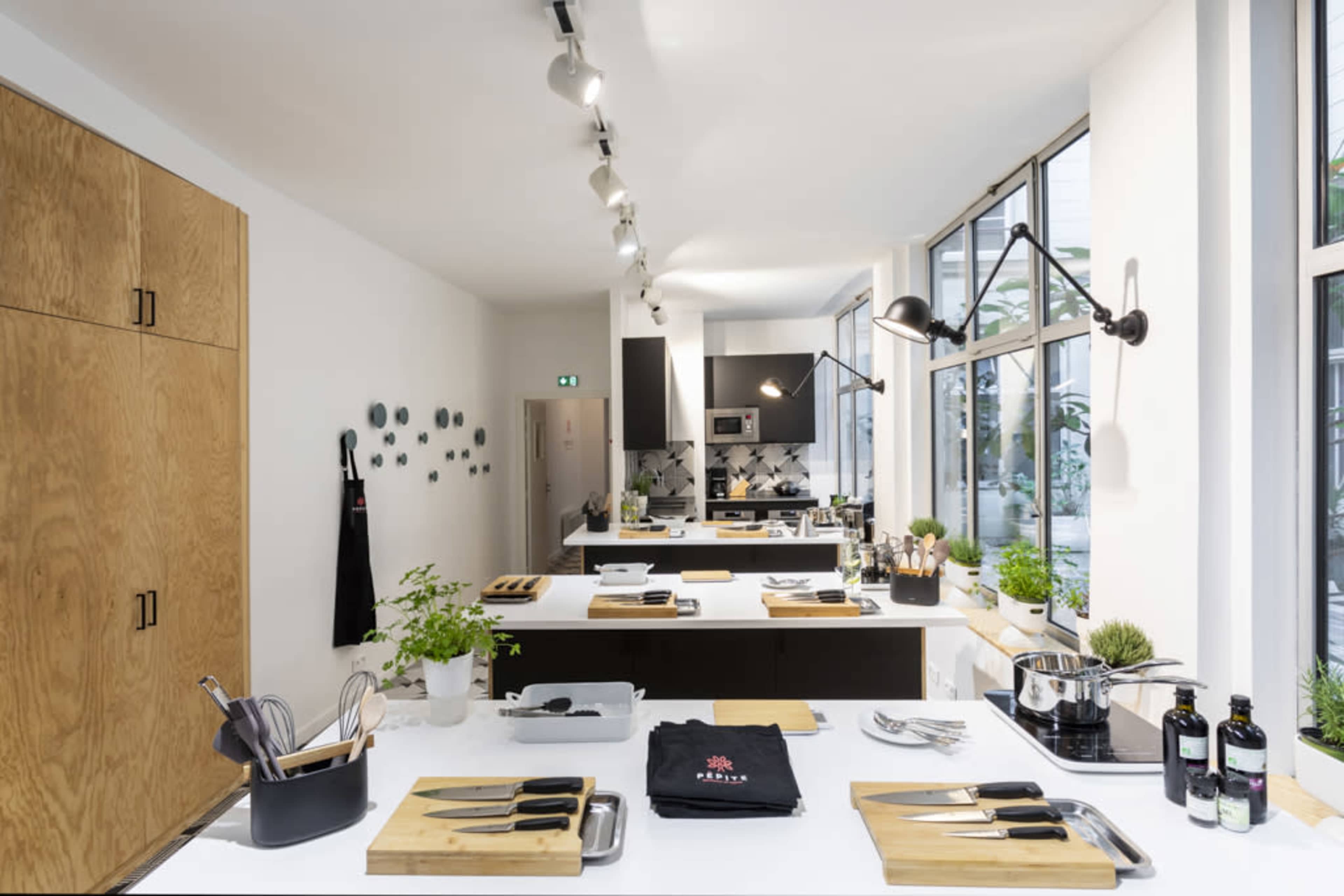 A modern kitchen with wooden cabinetry and multiple cooking stations equipped with utensils, knives, and potted plants.