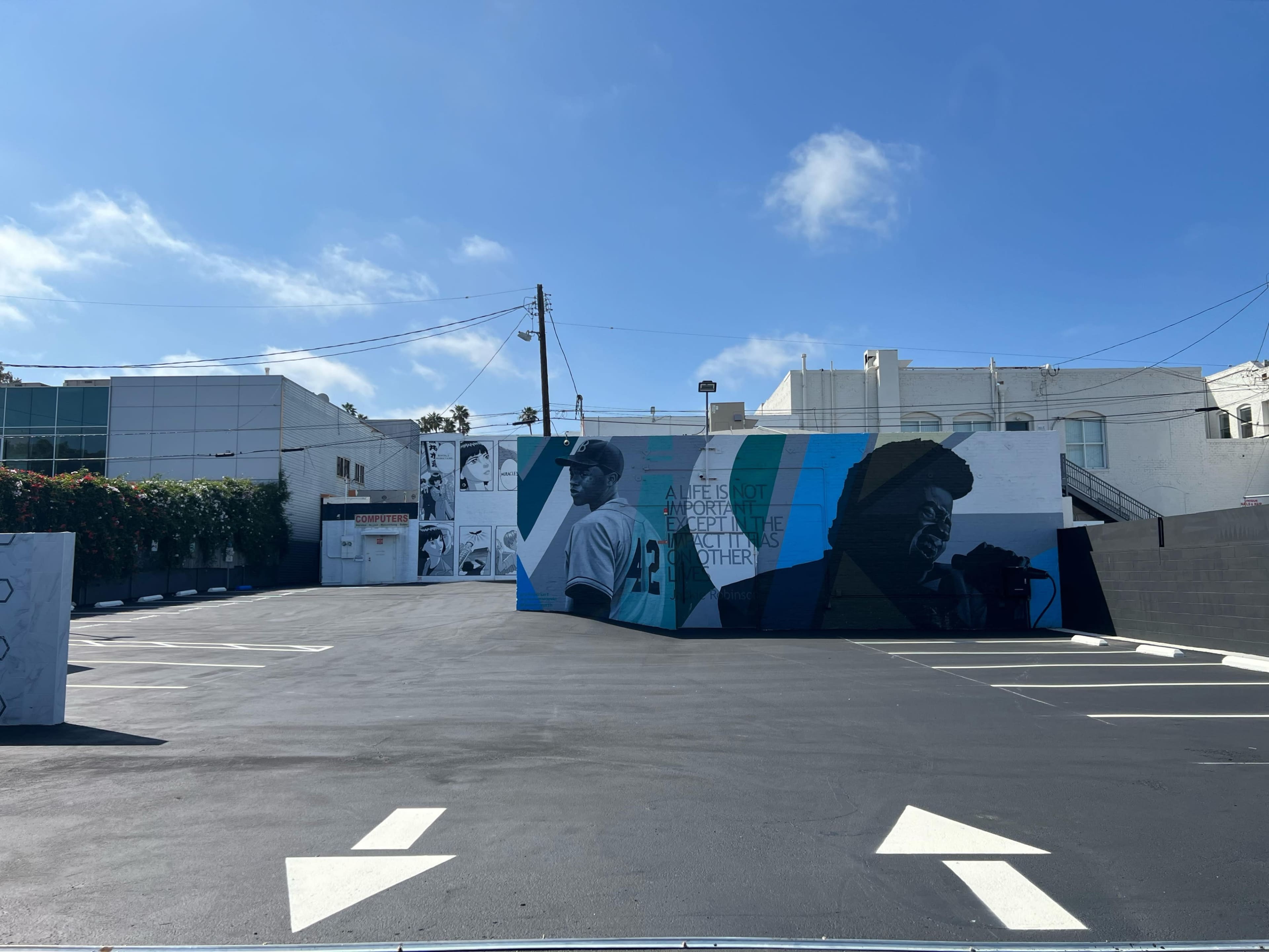 A parking lot with a large mural on the wall depicting two figures against a backdrop of blue and green.