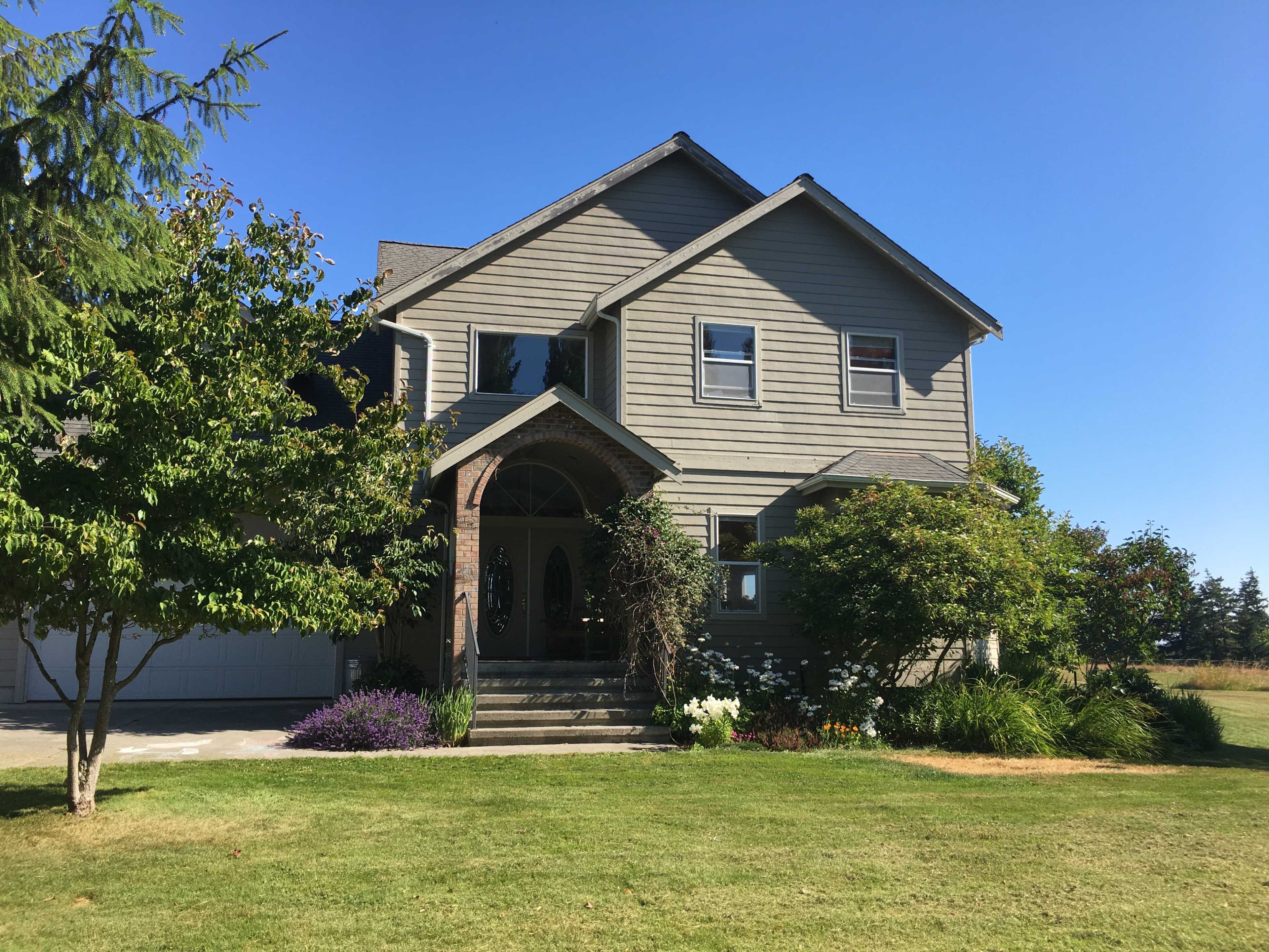 A two-story gray house with a front porch and landscaped yard under a clear blue sky.