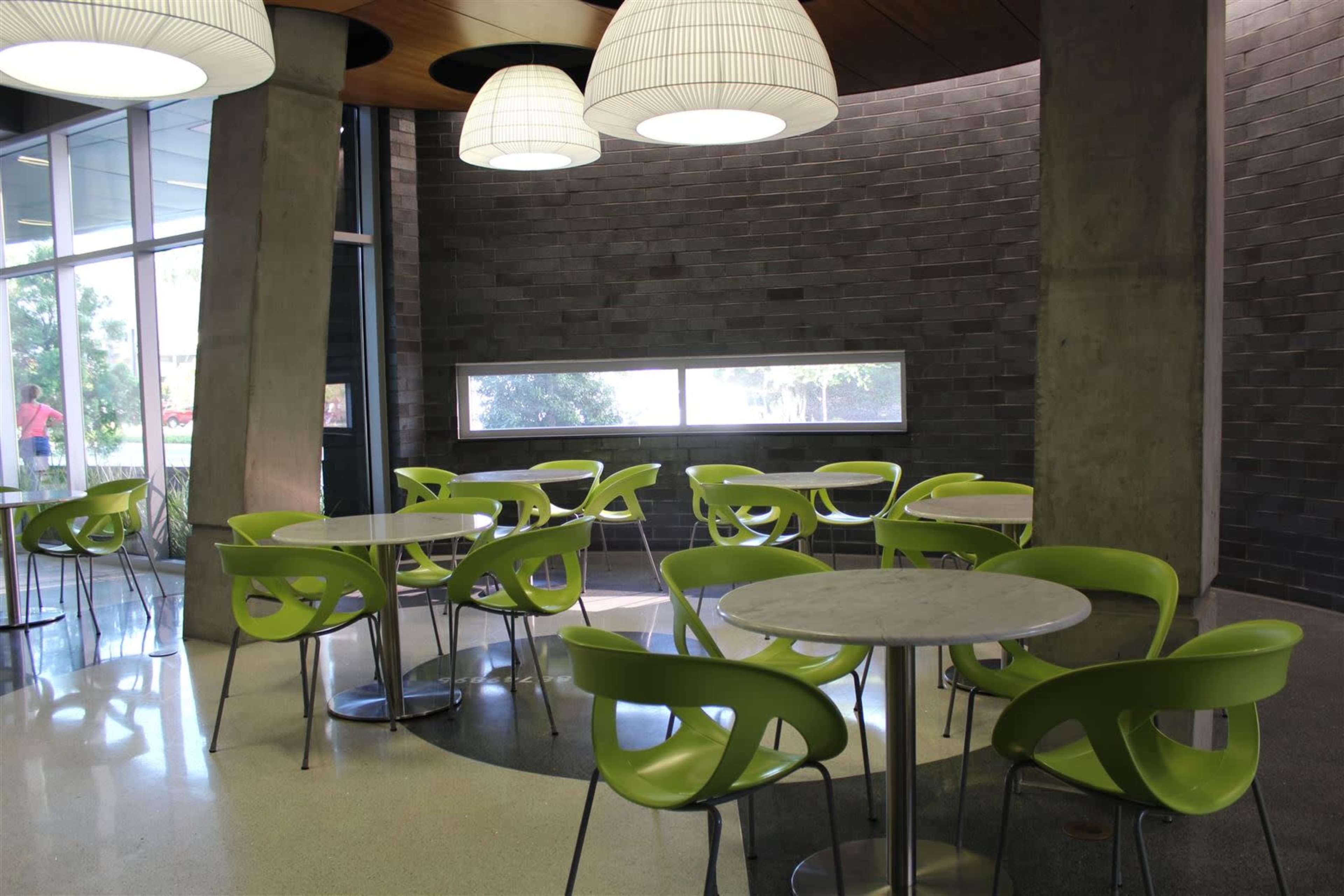 A modern coffee shop interior with several round tables and bright green chairs arranged around a well-lit space featuring large windows.