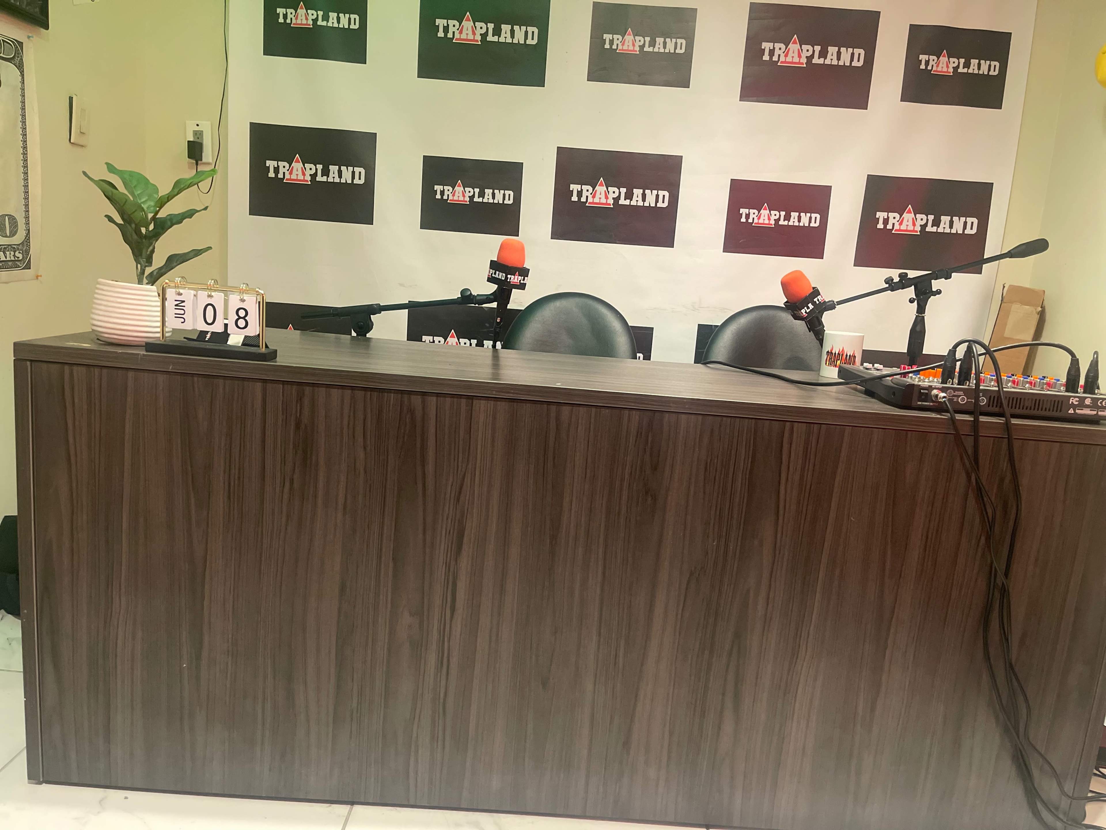 A studio desk with two black chairs and microphones, against a backdrop featuring the word "TRAPLAND."