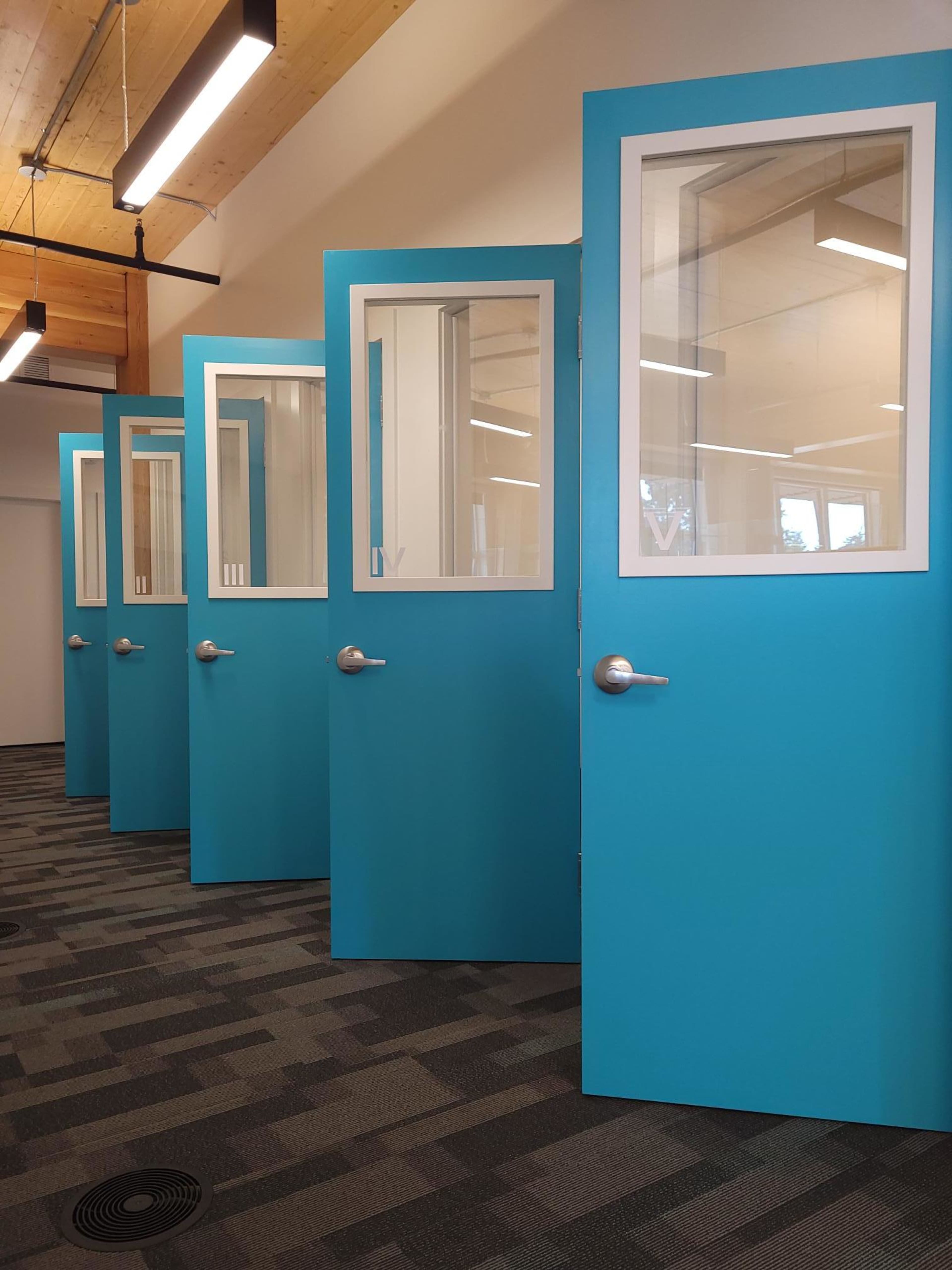 A row of five blue doors with glass panels is displayed in a modern office space.
