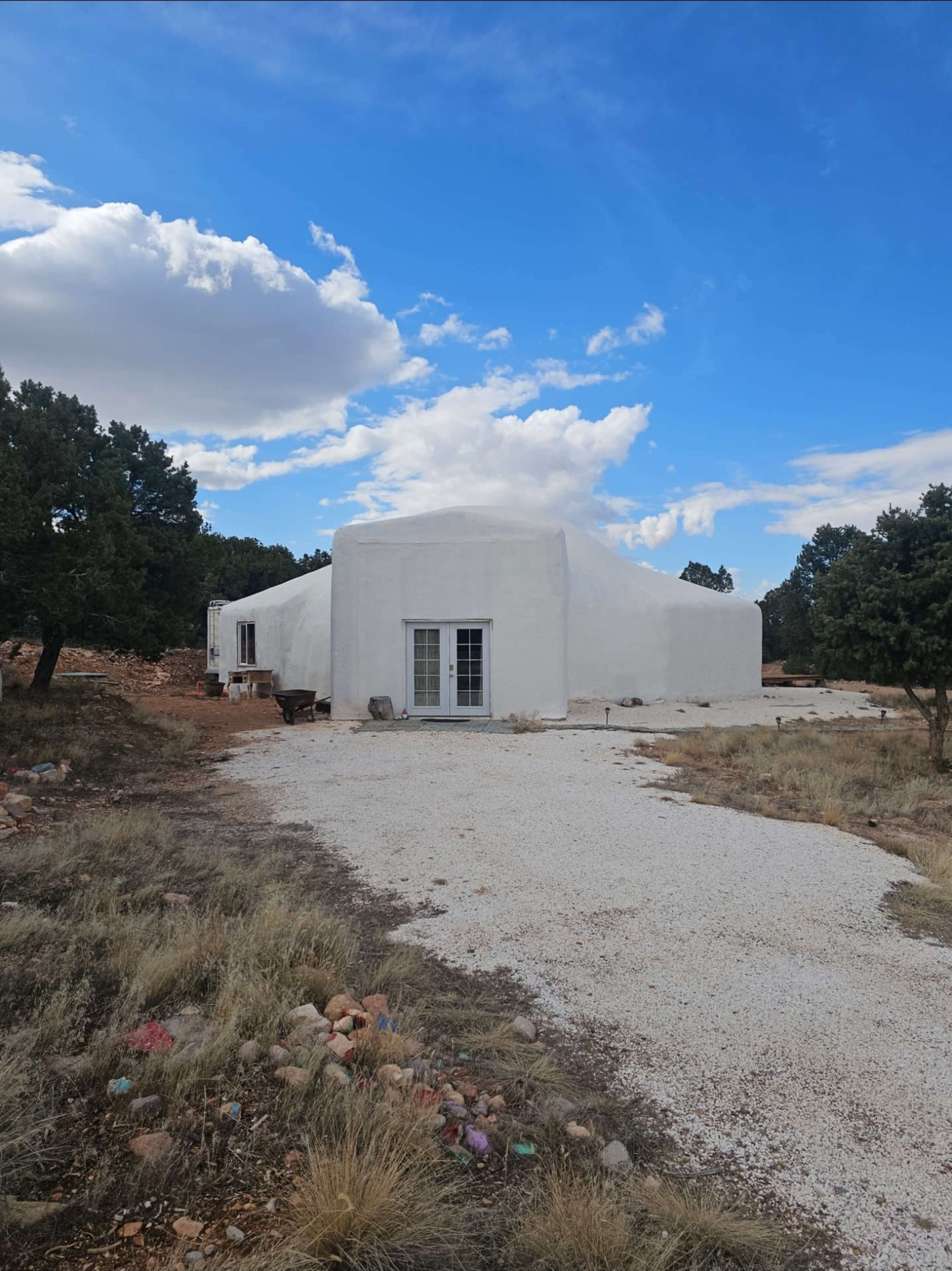 A white dome-shaped structure is set in a rocky landscape with sparse vegetation under a partly cloudy sky.